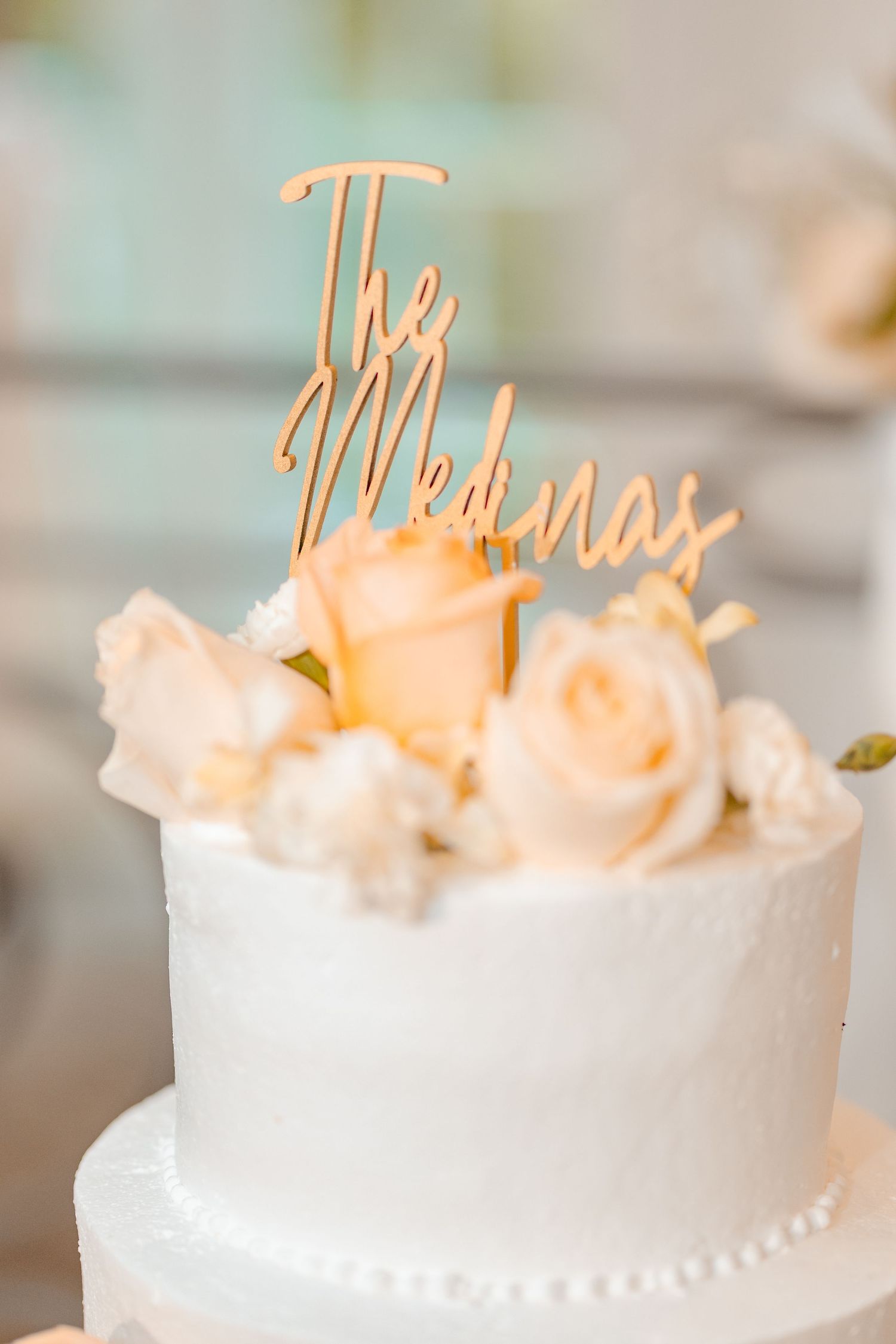 White wedding cake topped with gold laser-cut The Medinas topper and blush peach roses.