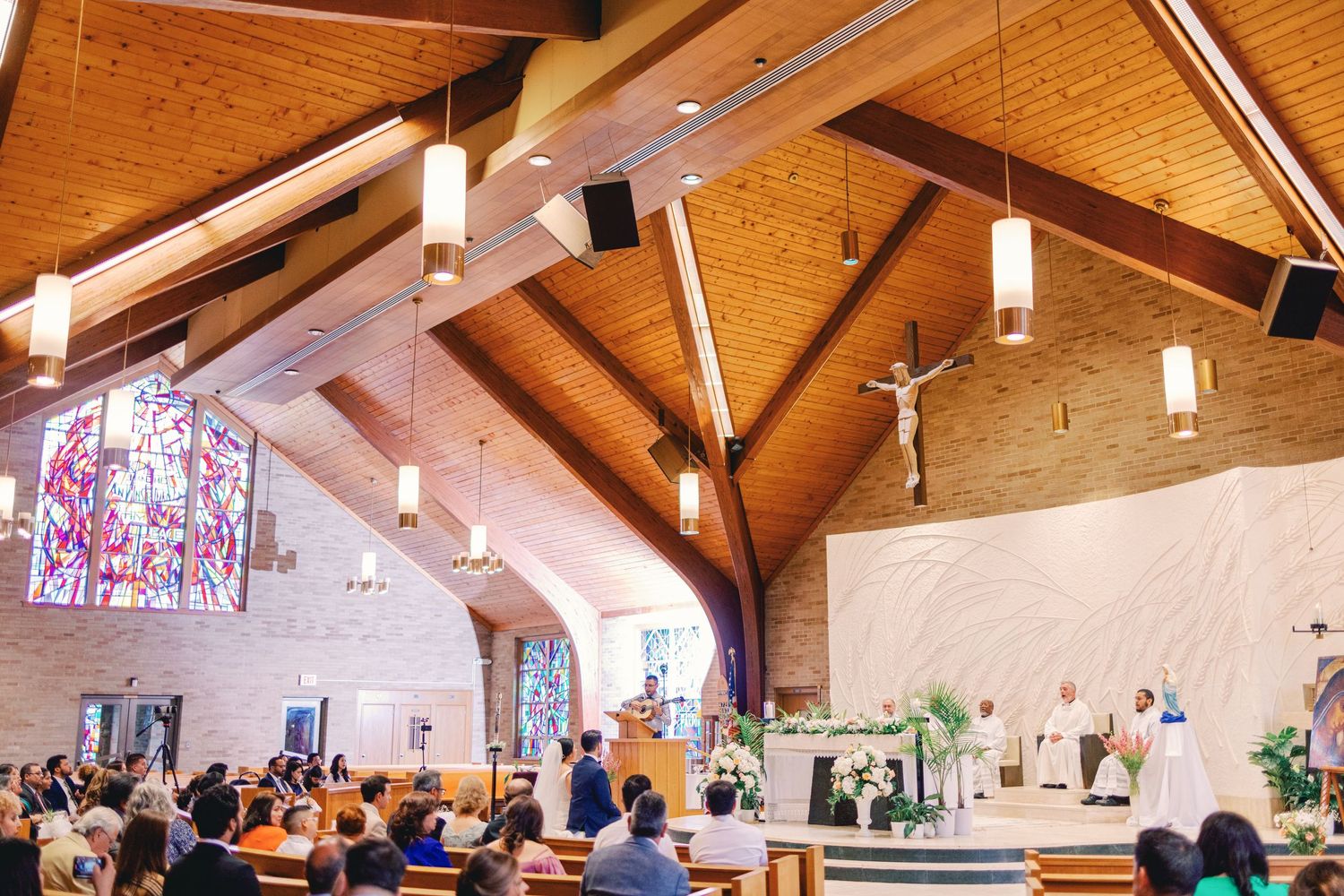 Wide view of a wedding ceremony inside a modern church with wood ceiling and stained glass windows.