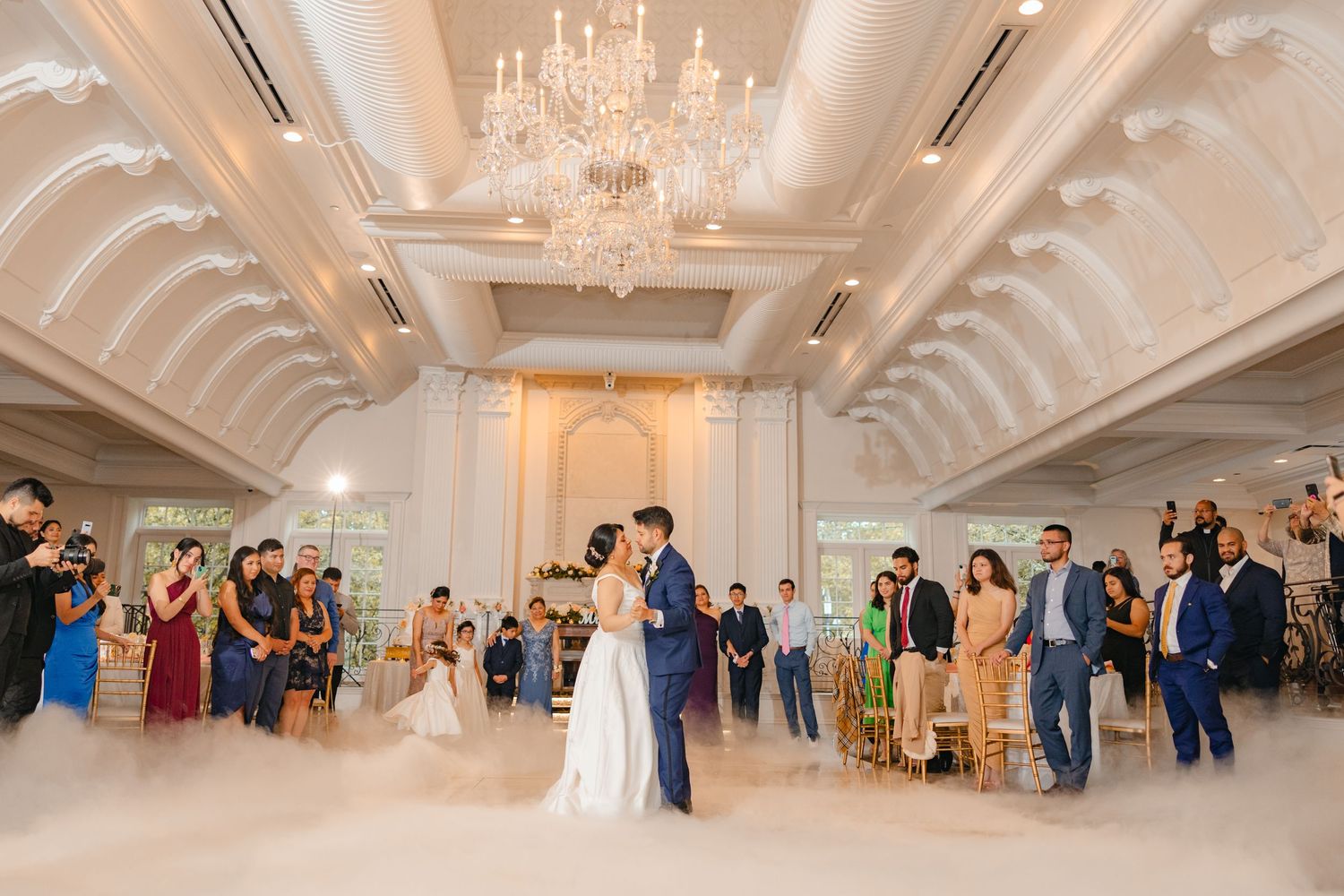 Bride and groom share their first dance on a cloud-filled dance floor in an elegant ballroom.