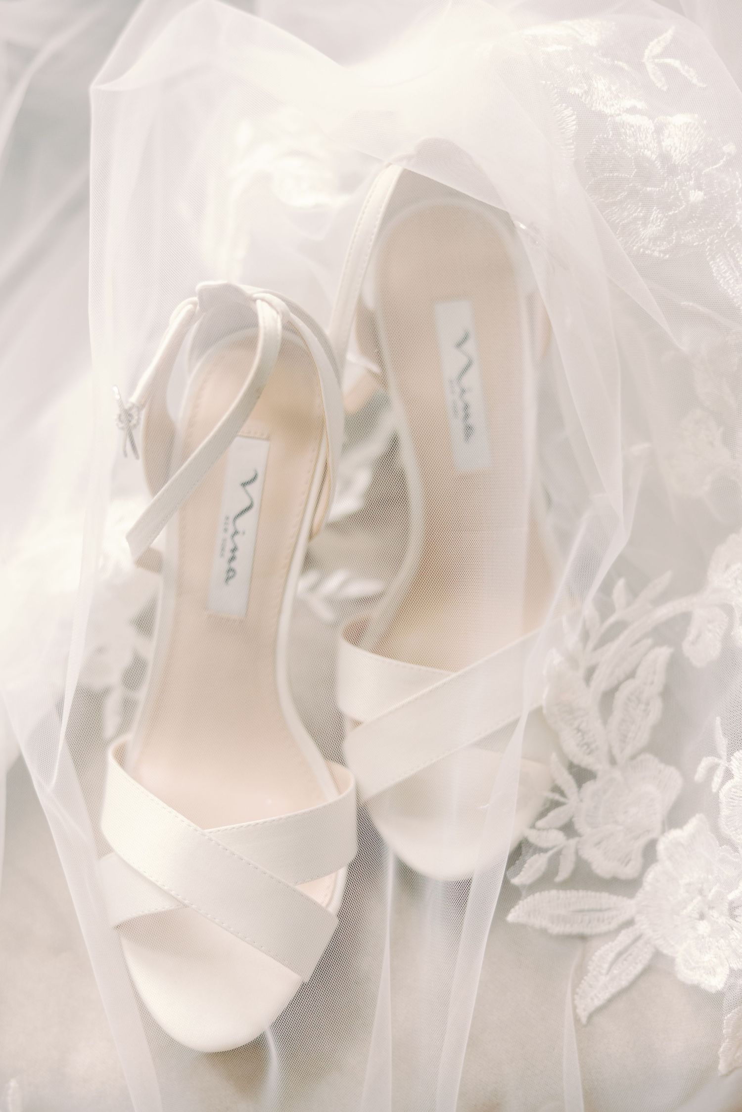 White satin bridal heels by Nina resting on a delicate lace wedding veil.