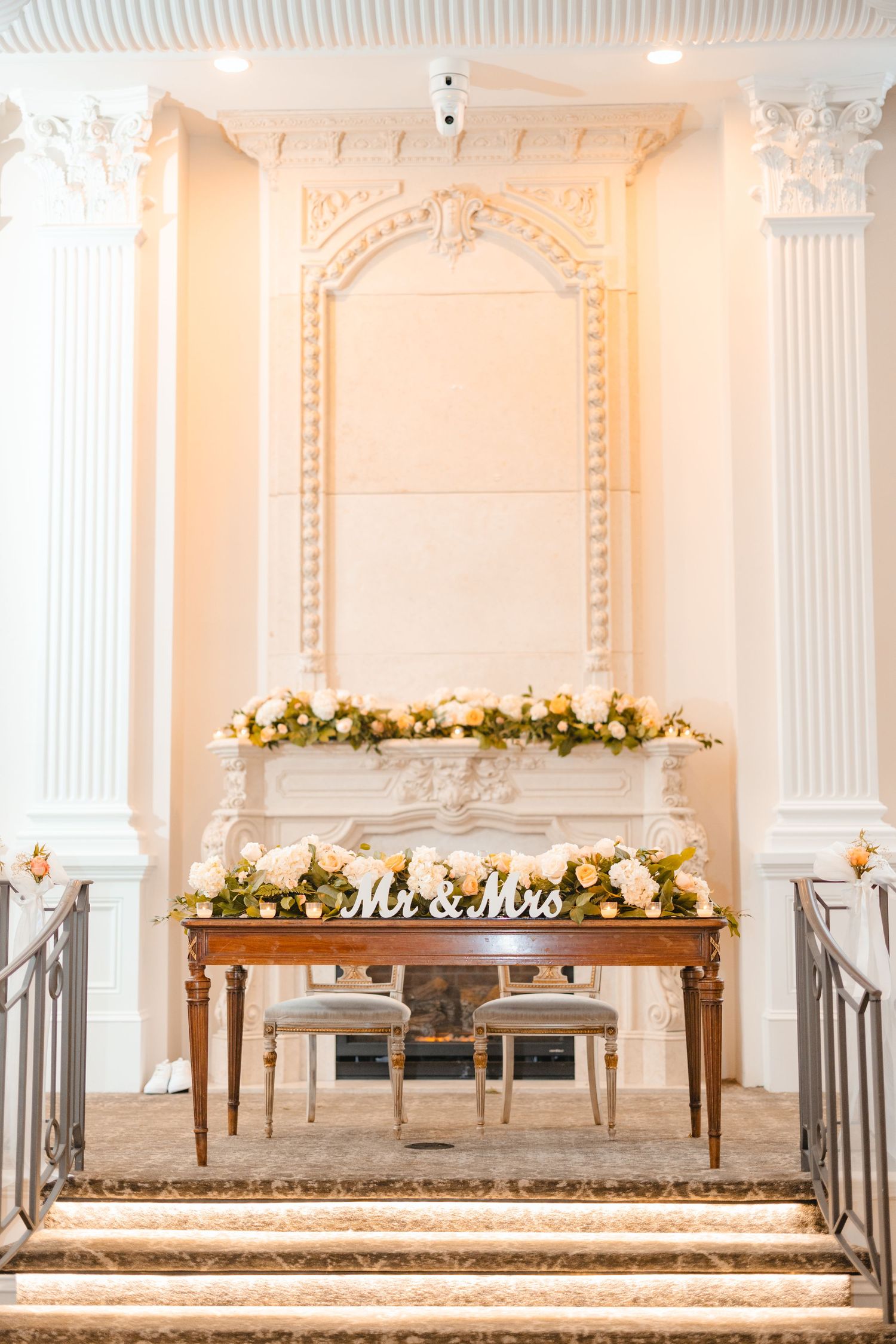 Elegant Mr and Mrs sweetheart table with floral garland in front of an ornate white fireplace.