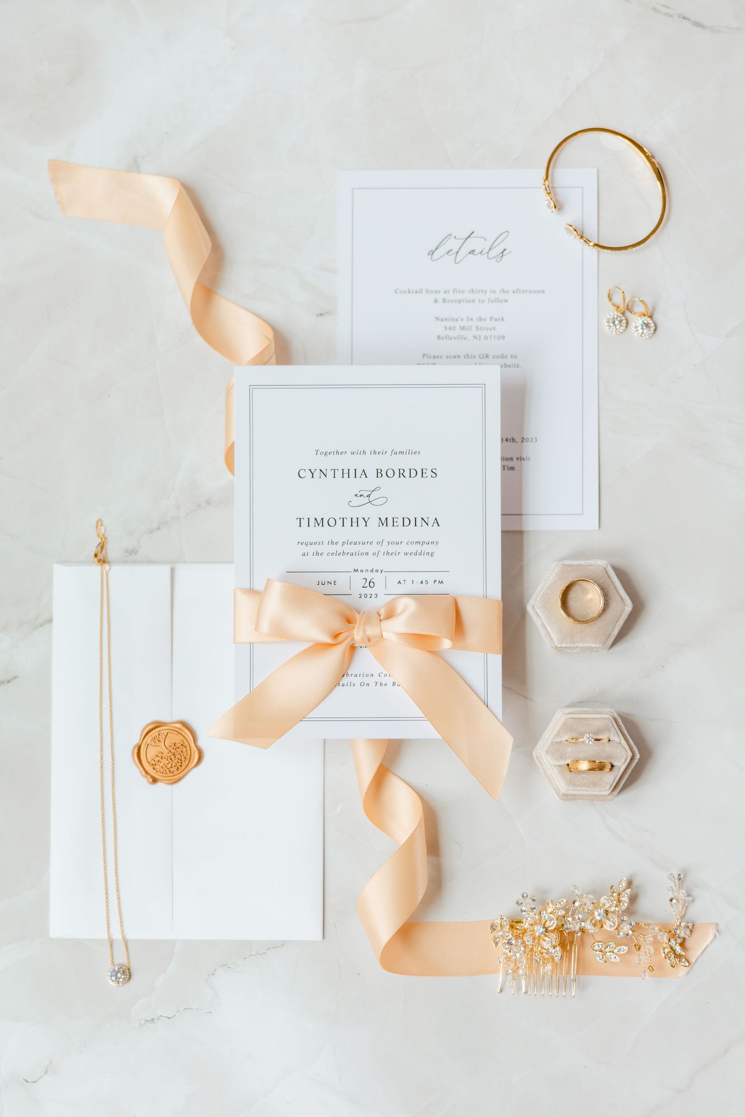 Elegant wedding invitation flat lay for Cynthia Bordes and Timothy Medina with peach ribbon and gold accessories.