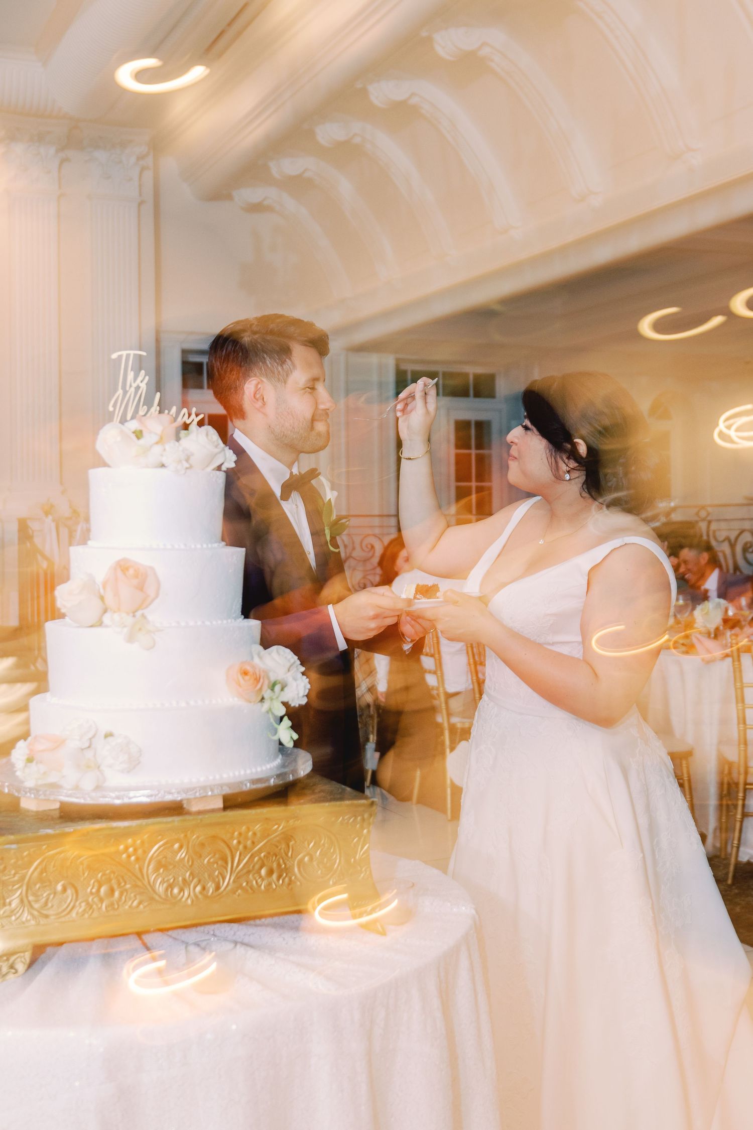 Bride and groom cut their white tiered wedding cake in a softly lit elegant reception hall.