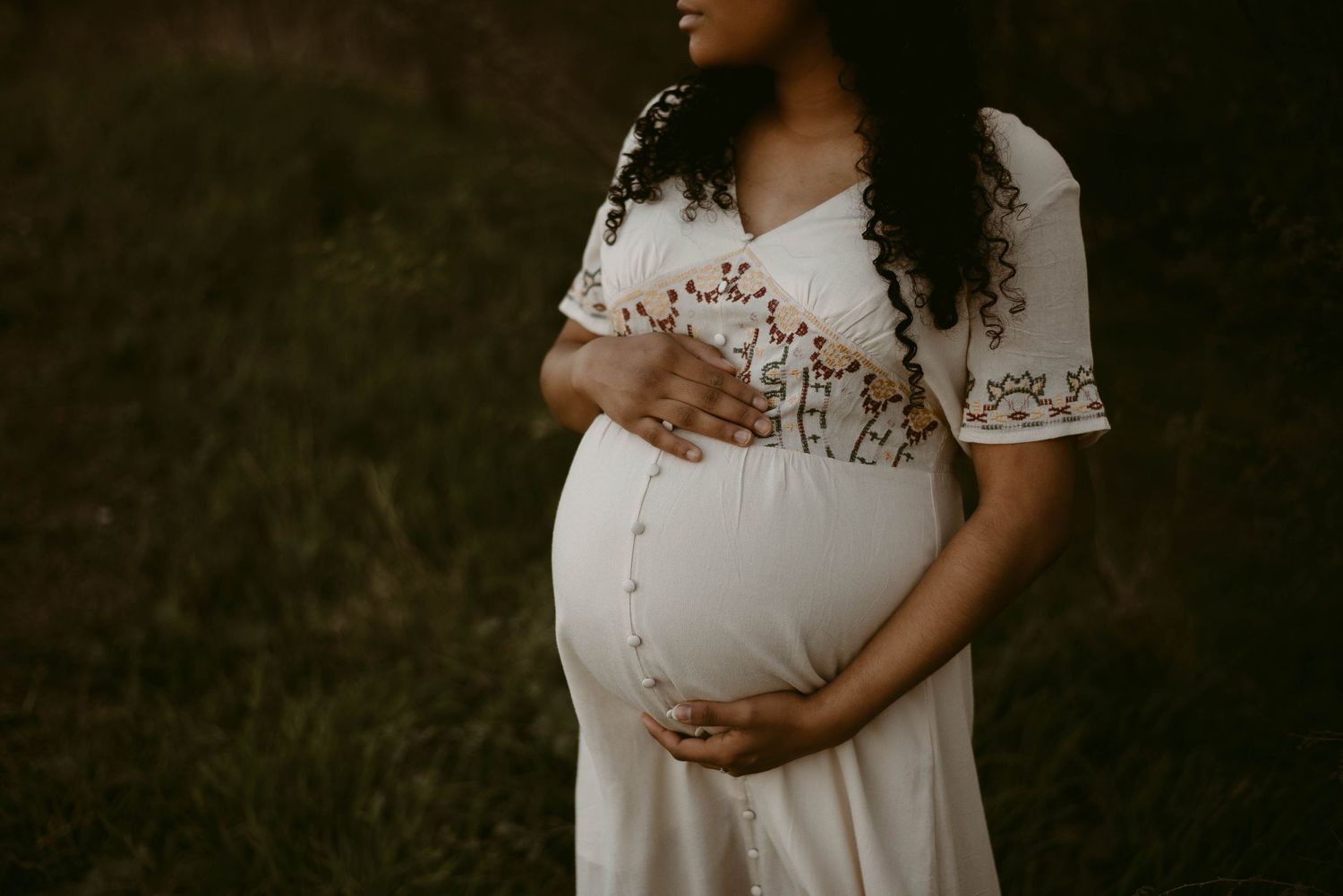 Close-up maternity portrait highlighting embroidered details on a white dress.