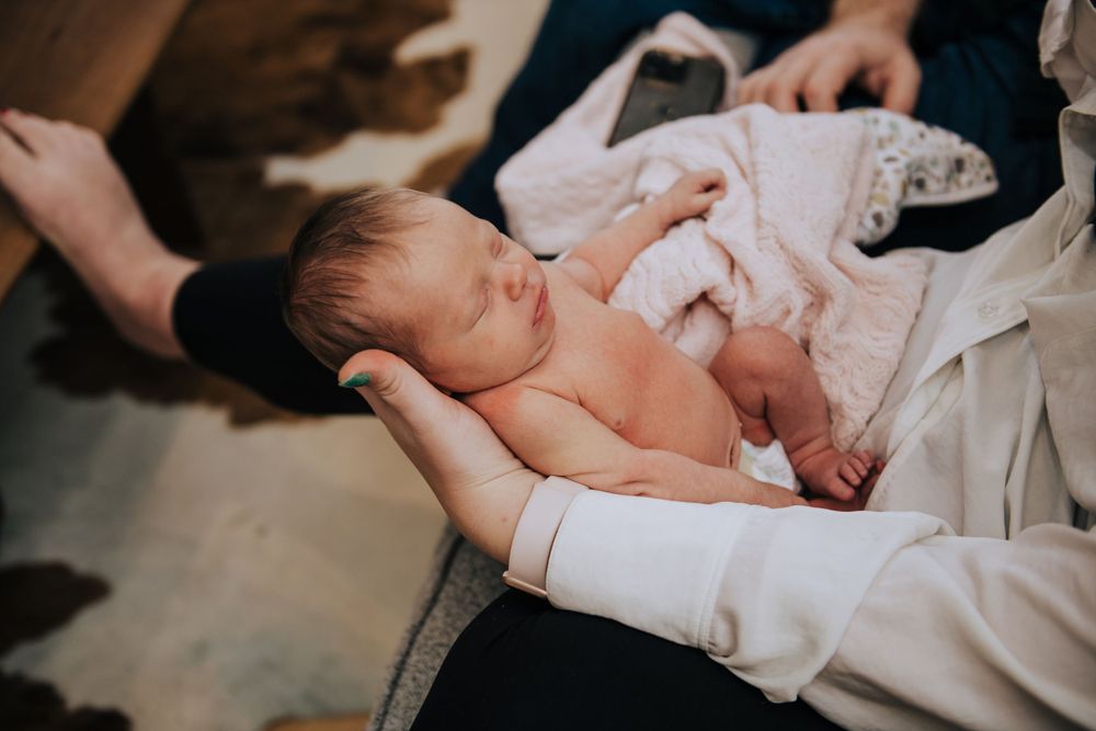Gentle hands supporting a sleeping newborn in soft lighting.