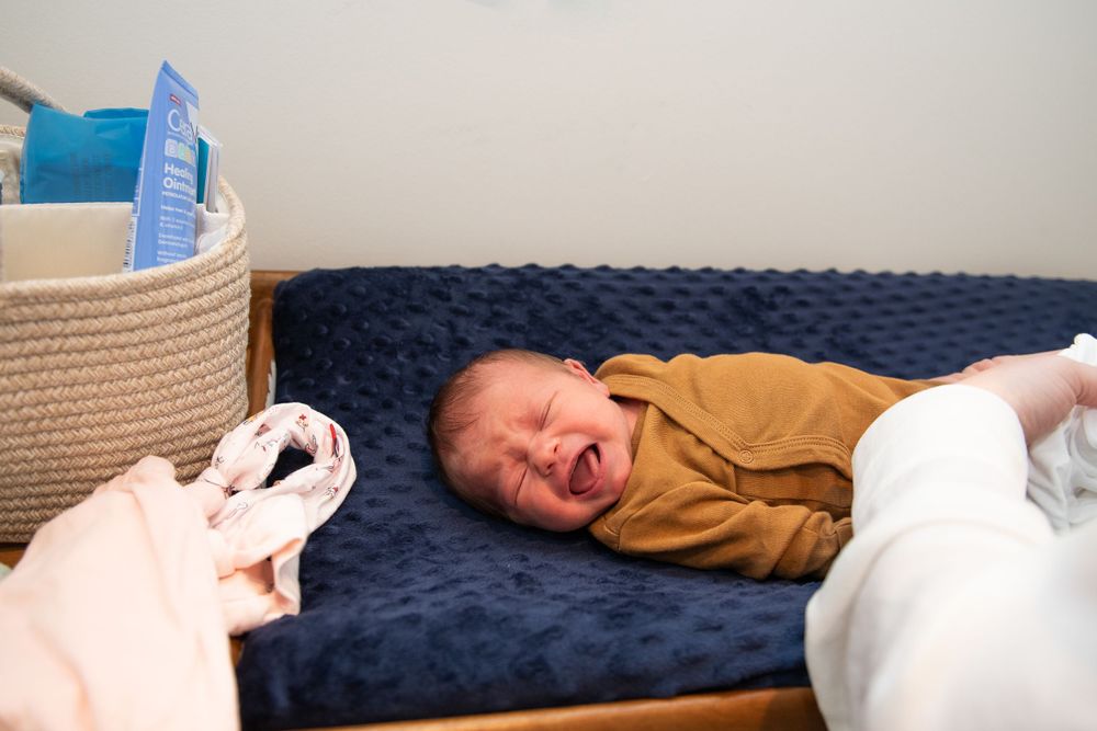 Newborn baby in brown onesie crying while lying on dark blue cushion.