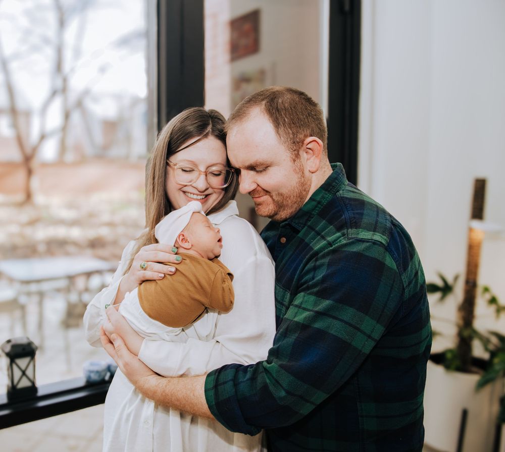 Family bonding with newborn baby by window in cozy home setting.