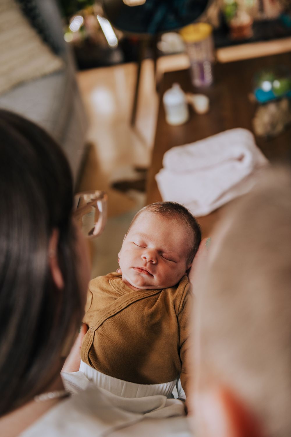 Sleeping newborn in brown outfit being cradled during photography session.