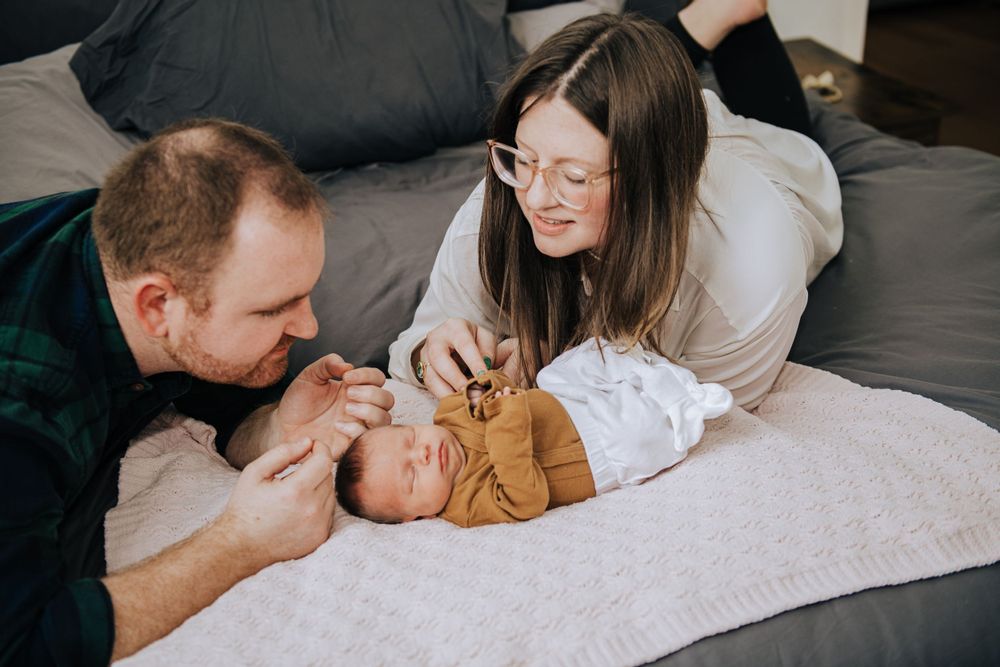 Parents lying on bed gently interacting with their newborn baby.
