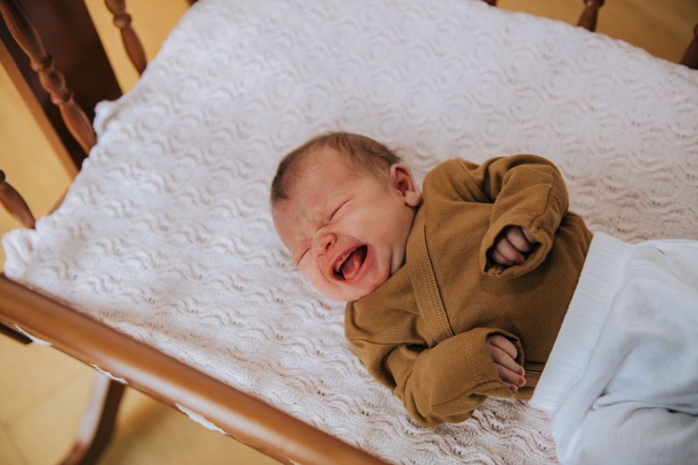 Laughing baby in brown outfit on white quilted surface.