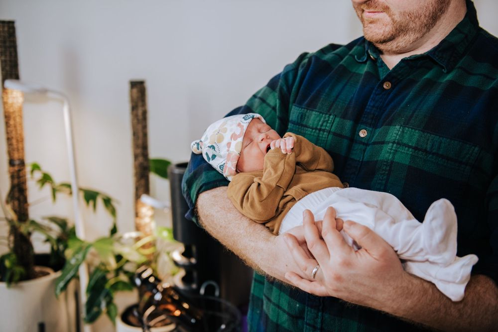 Newborn baby sleeping in caregiver's arms wearing brown and white outfit.