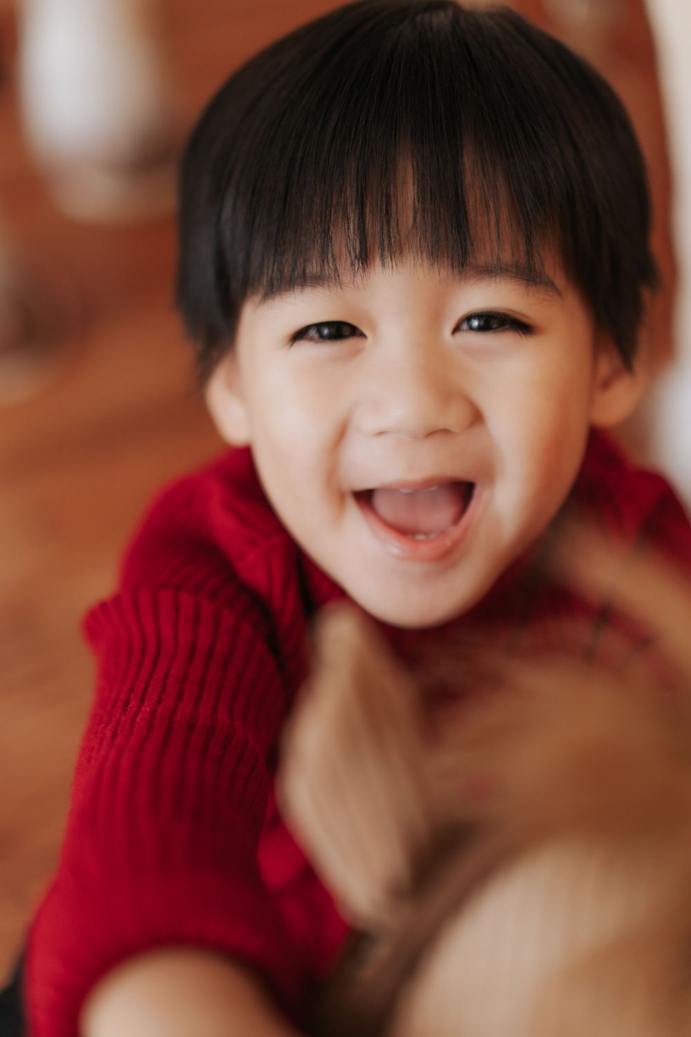 Joyful toddler in red sweater laughs with a bright smile against warm background.
