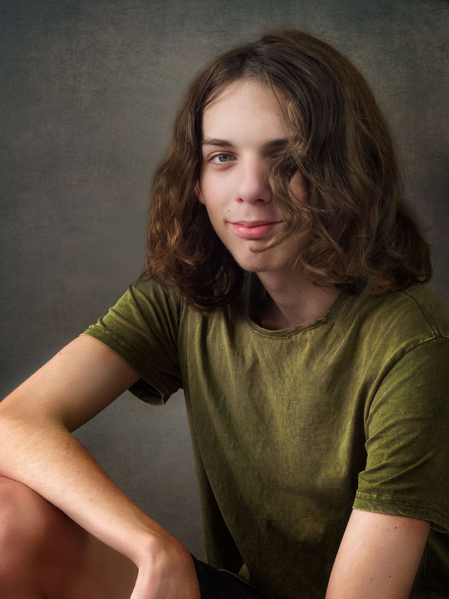Teen Male Portait with long brown hair in a casual sitting postion wearing a green tshirt