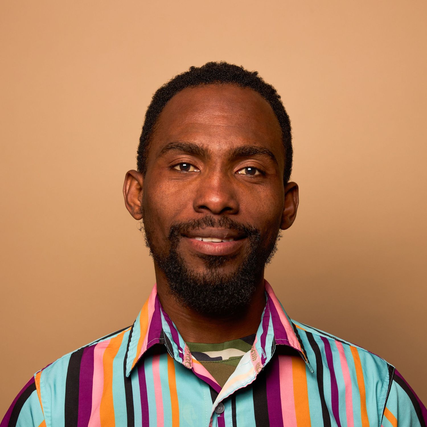 Professional headshot of person in colorful striped shirt against warm brown background.