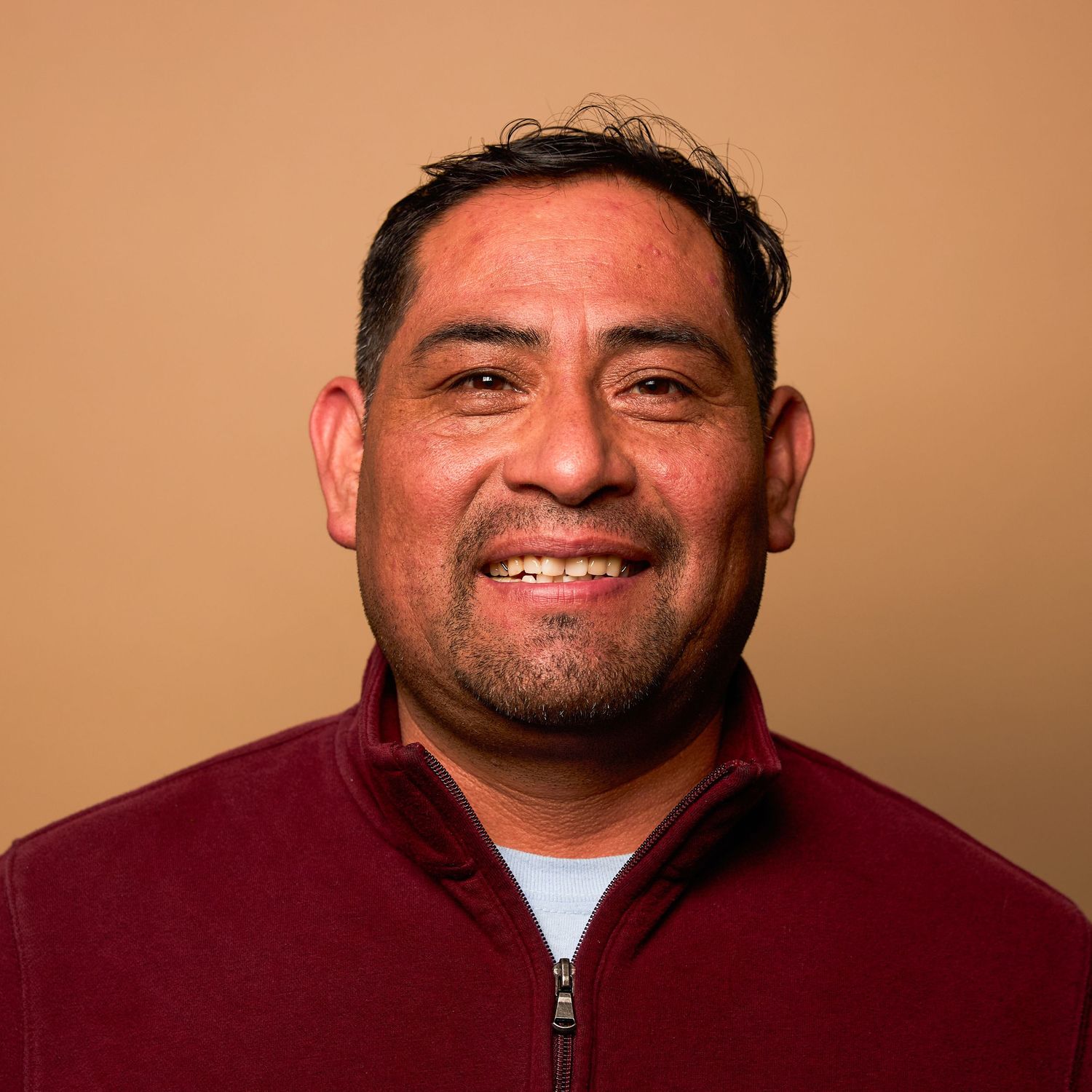 Cheerful person in burgundy quarter-zip pullover photographed against brown background.