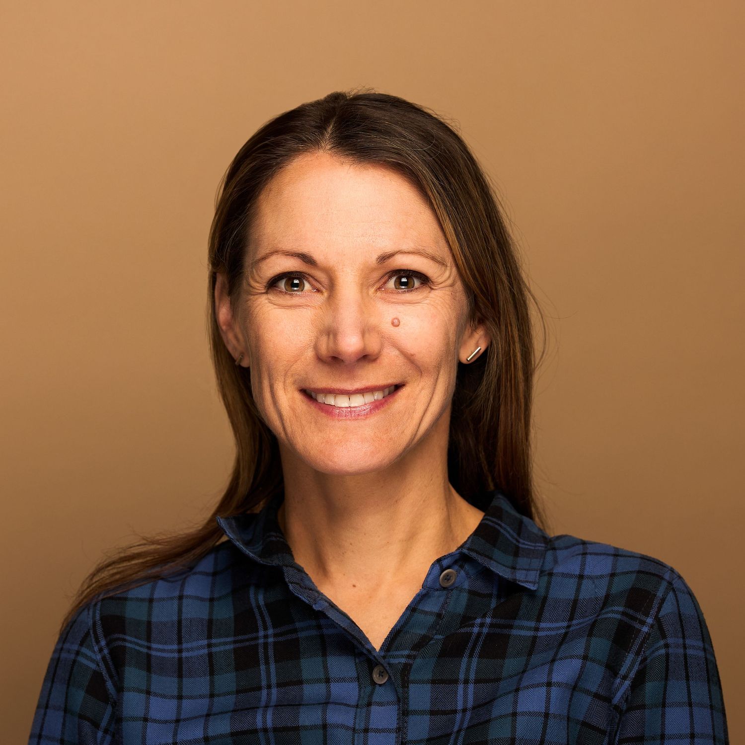 Professional headshot of person wearing plaid button-up shirt against brown background.