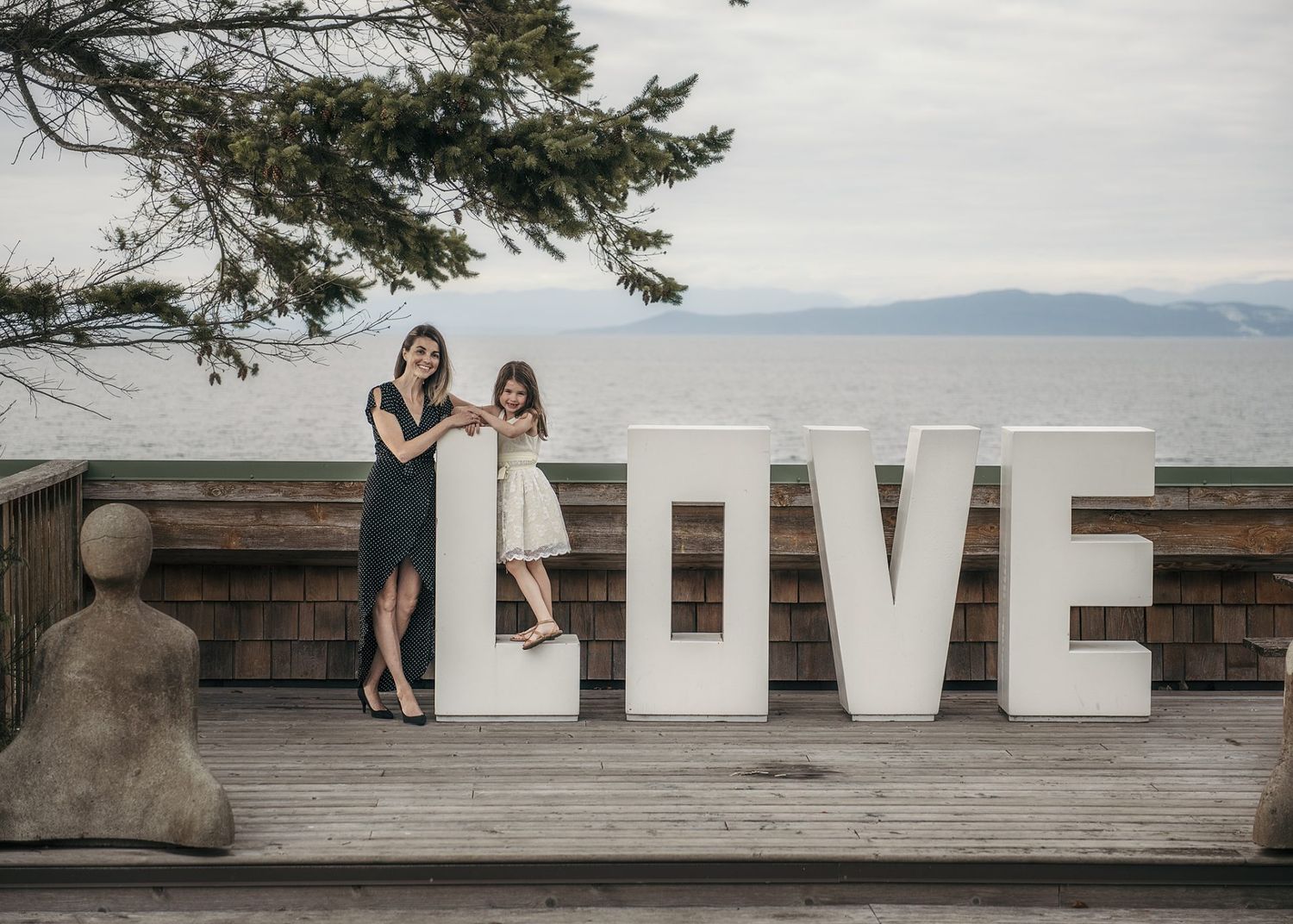 White LOVE letters displayed on wooden deck overlooking mountain lake with scenic backdrop.