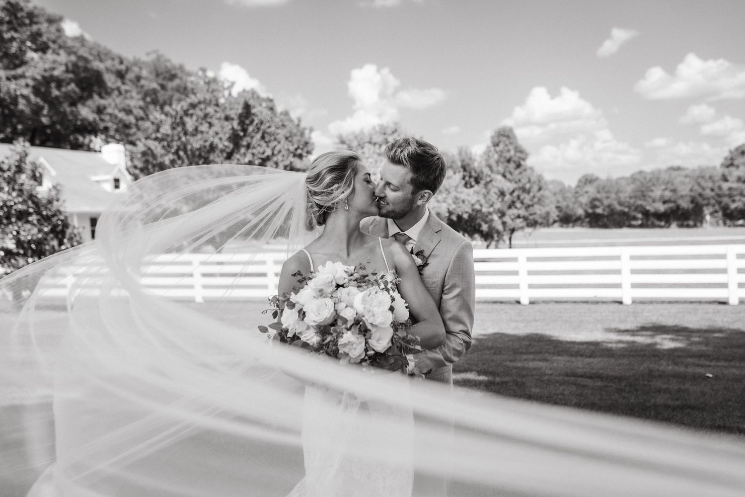 Black and white wedding photo of a couple in front of a white fence on their special day.