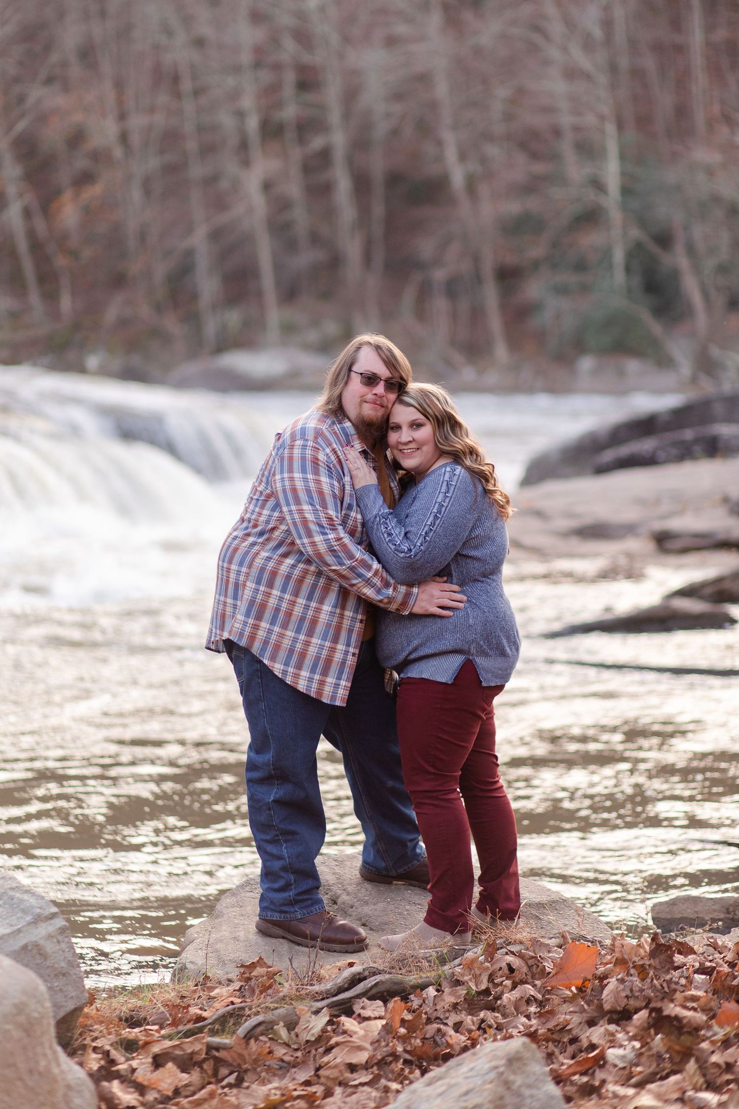 Two people share an intimate moment on rocky terrain near a waterfall.