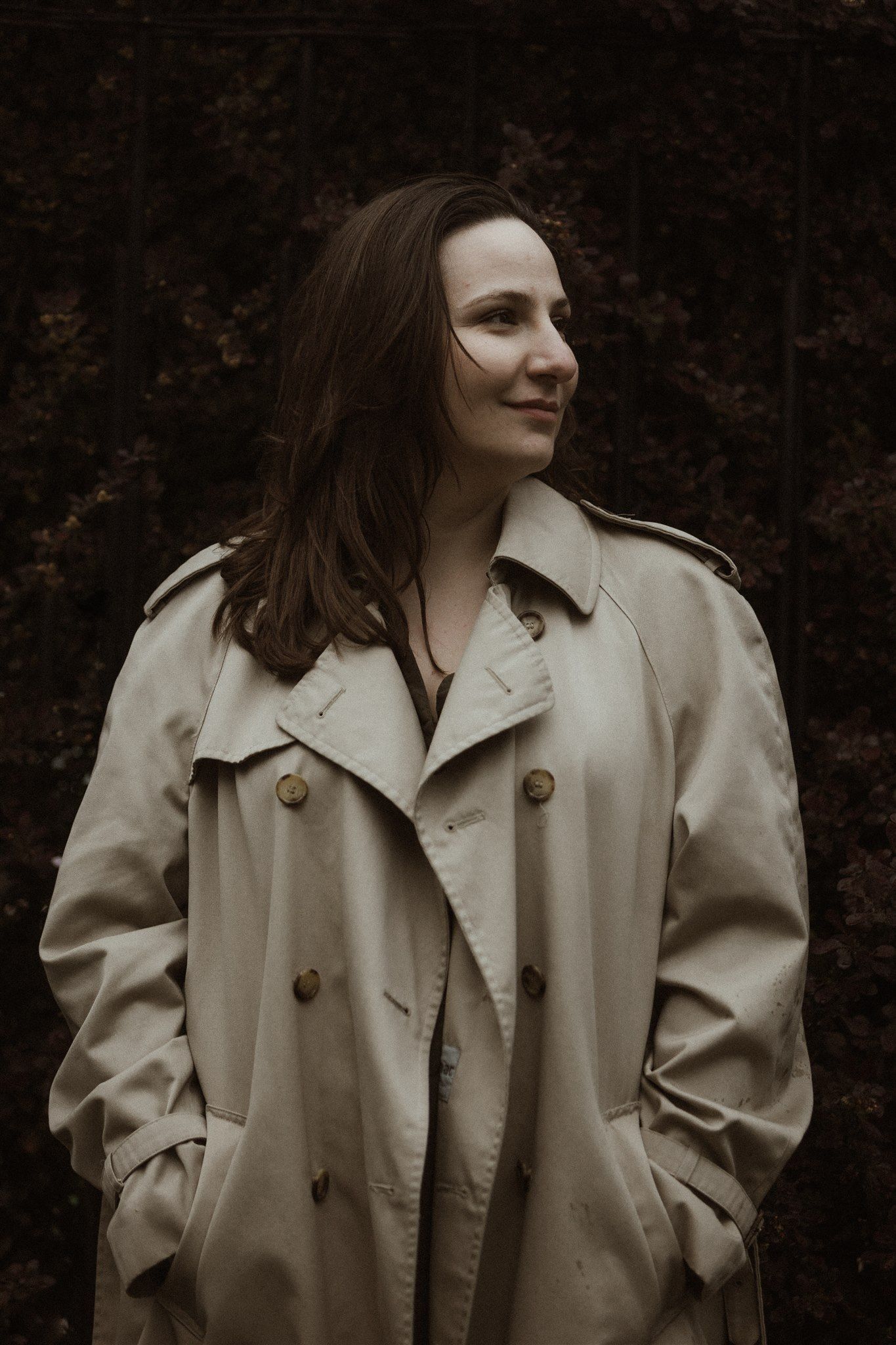 A portrait in sepia tones showcasing someone wearing a classic trench coat against autumn foliage.