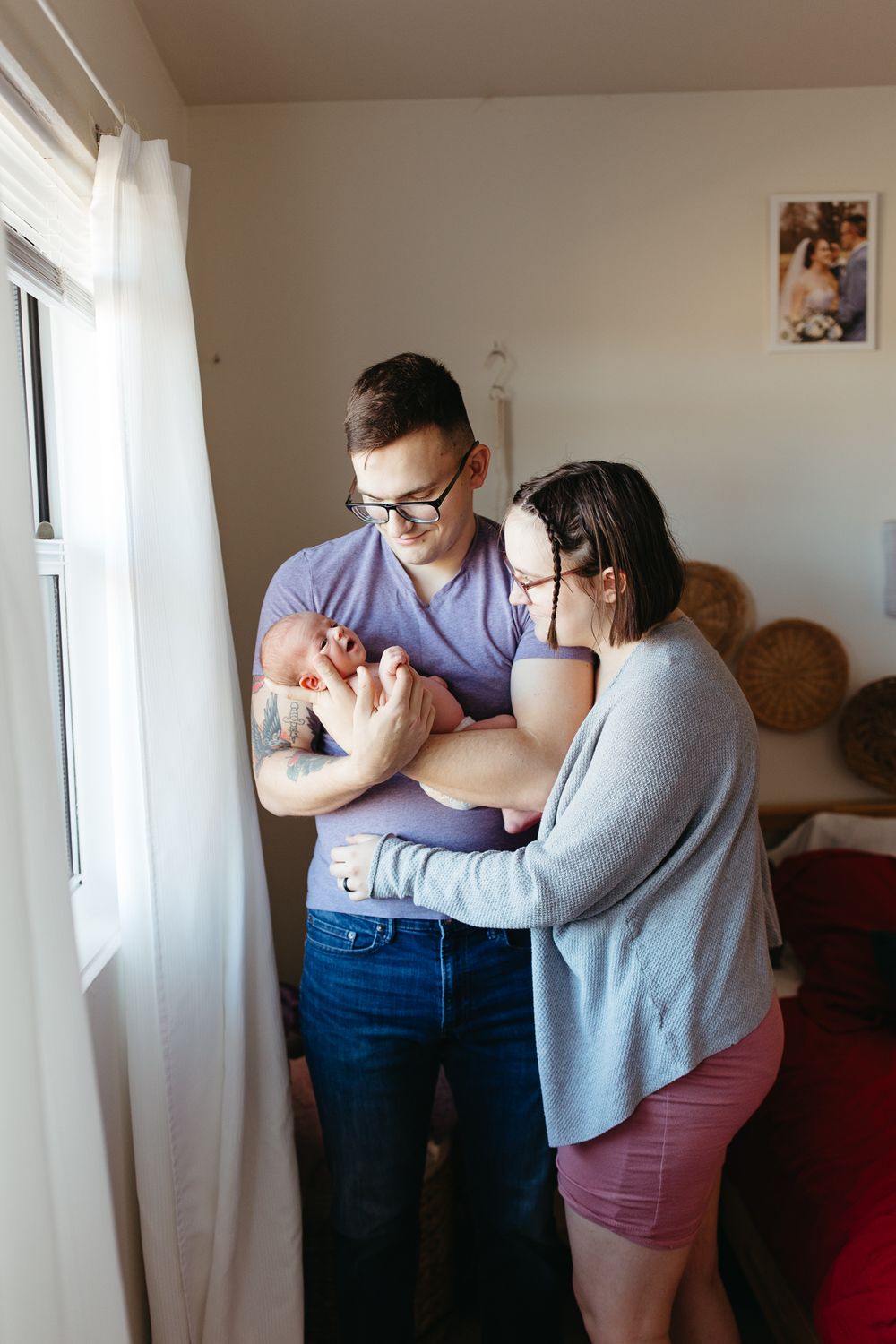 Parents standing by bright window gazing lovingly at their newborn baby.