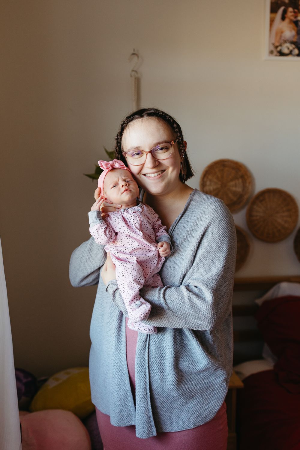 Parent in grey cardigan holding smiling newborn baby by window.