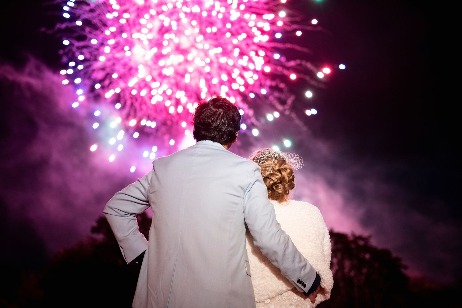 A couple watches pink fireworks display during their wedding celebration.