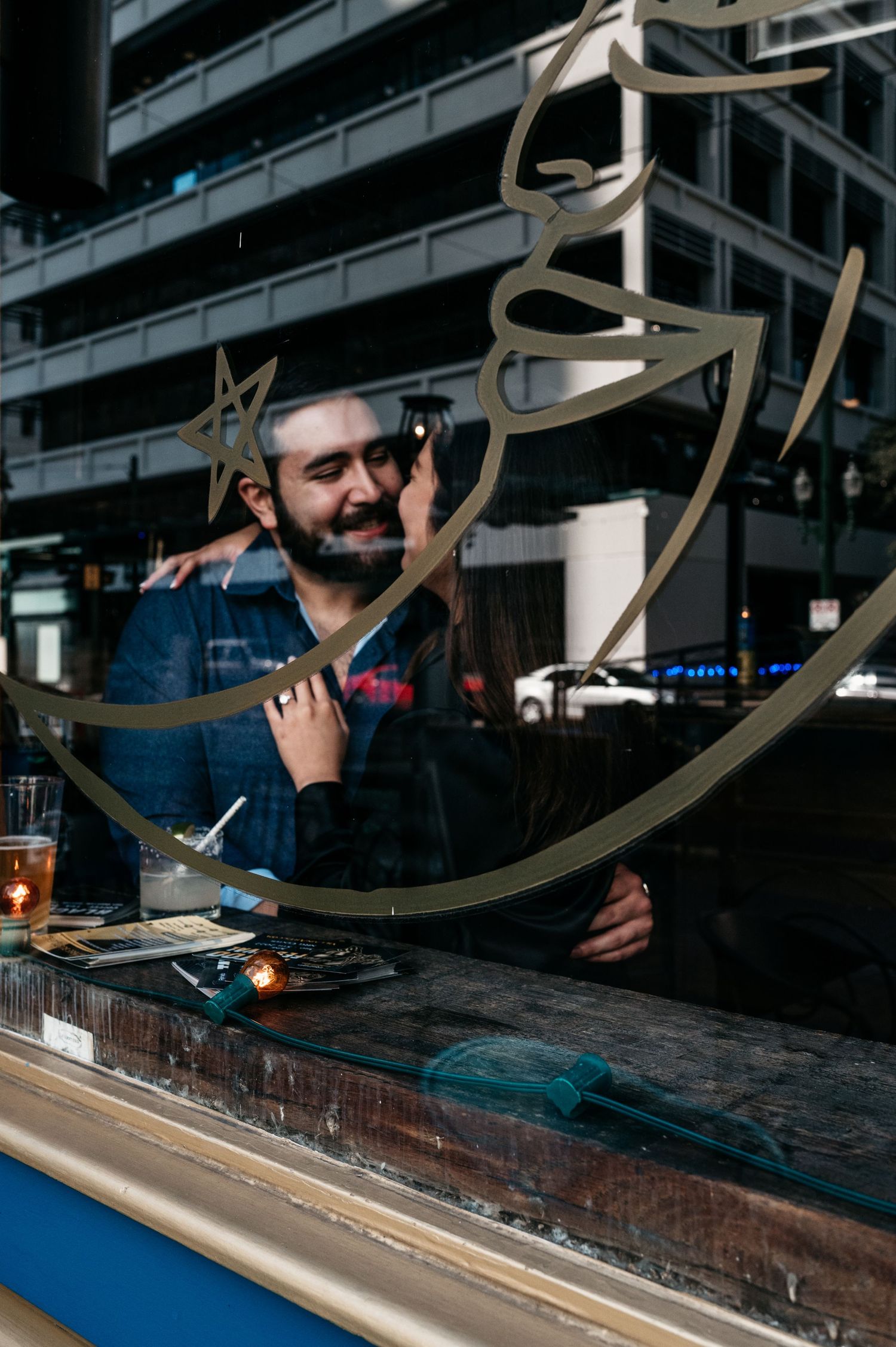 A reflection through a window shows a person at a bar counter.