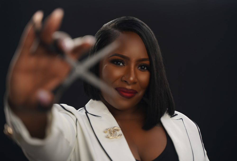 Professional portrait of someone in a white blazer reaching toward the camera against a dark background.