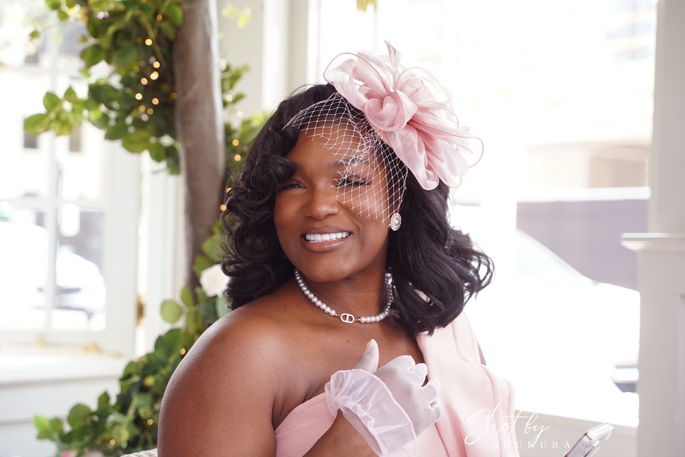 An elegant tea party portrait featuring a pink fascinator, pearls and formal attire.