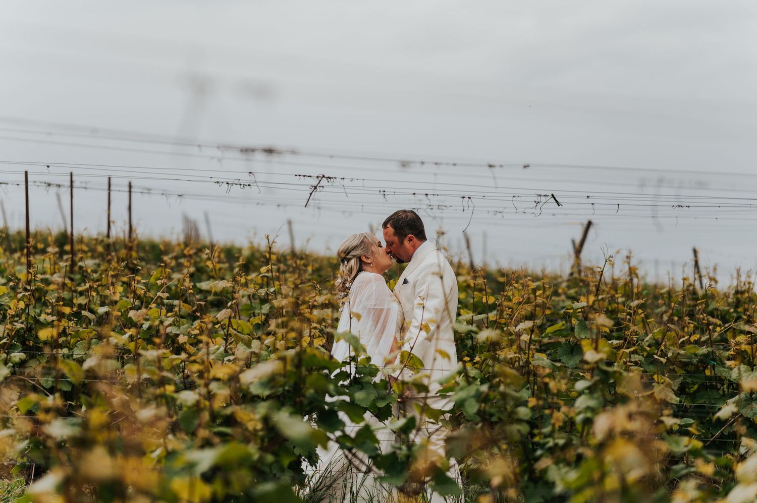 A couple strolls through a field of yellow wildflowers on a cloudy day.