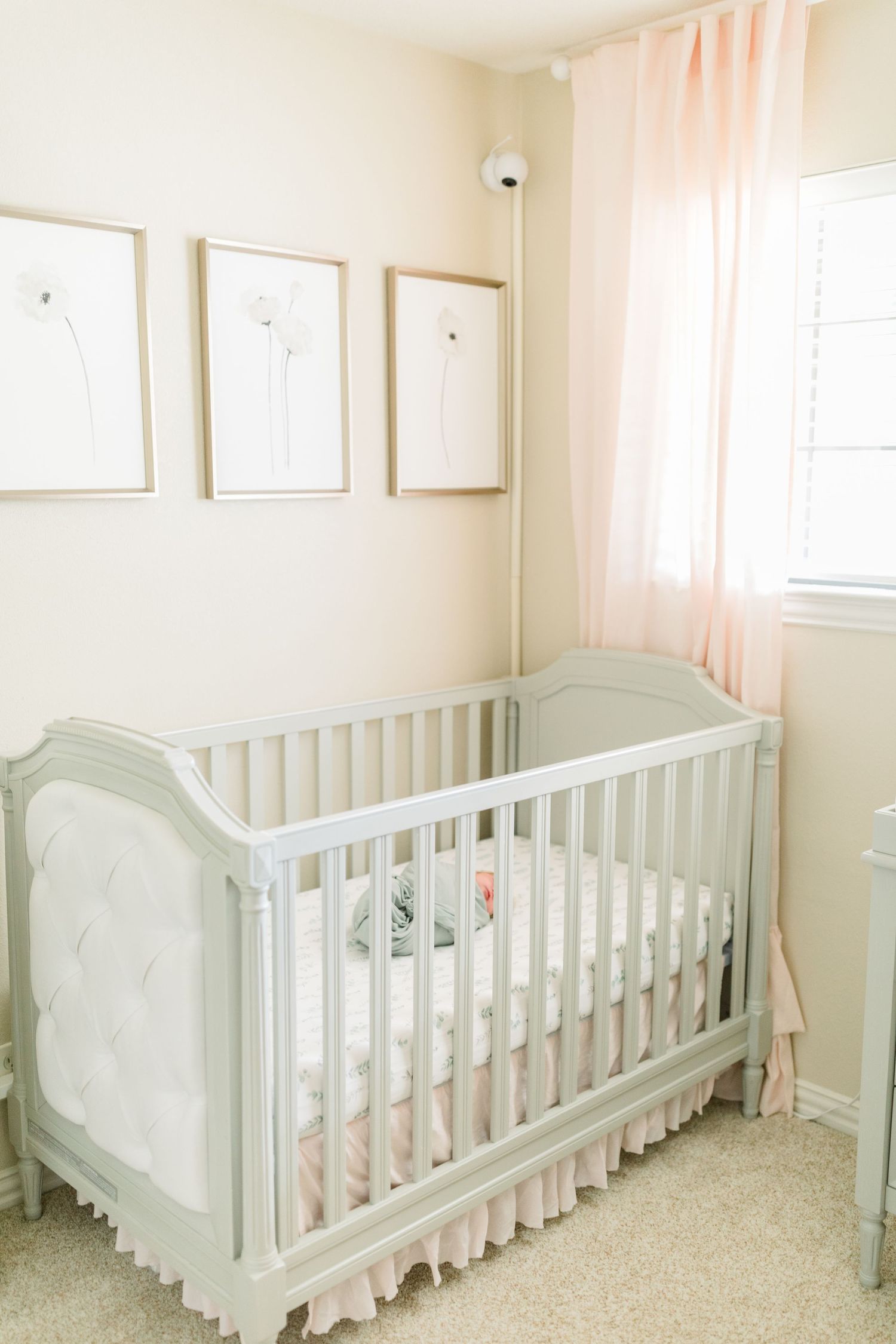 Minimalist nursery with white crib, pink curtains, and simple framed wall art.