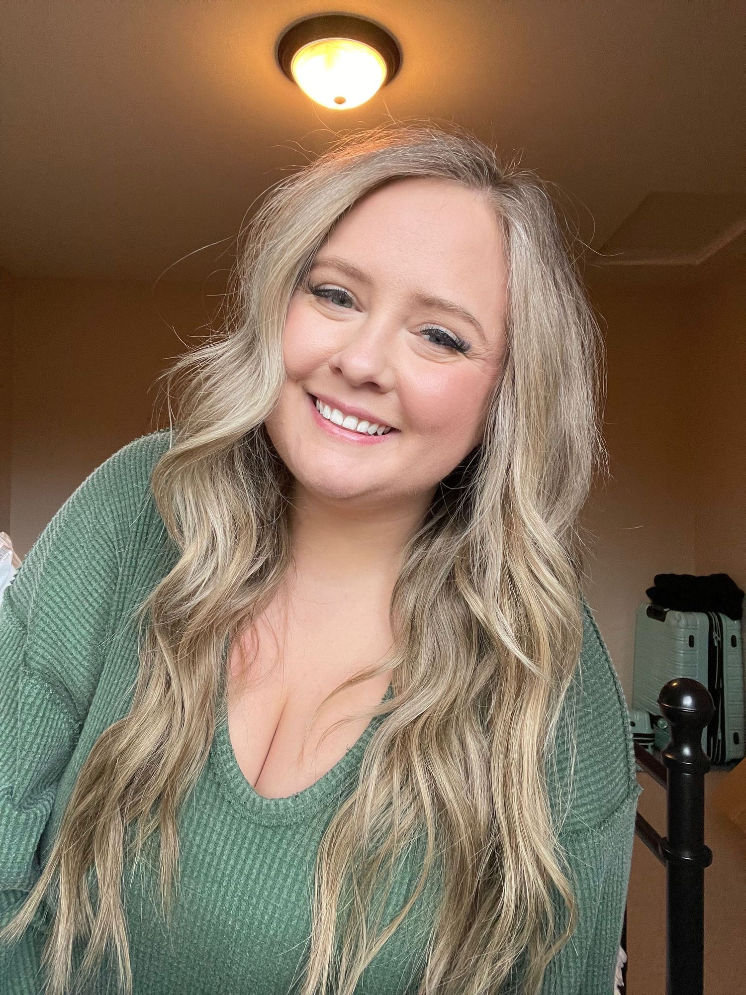 A person in a green sweater smiling warmly at the camera in indoor lighting.