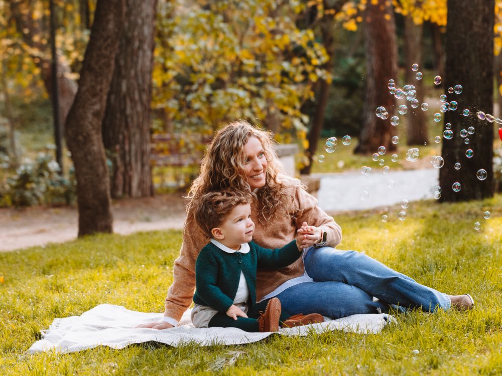 Family and dogs enjoying a playful moment on a picnic blanket in a park.