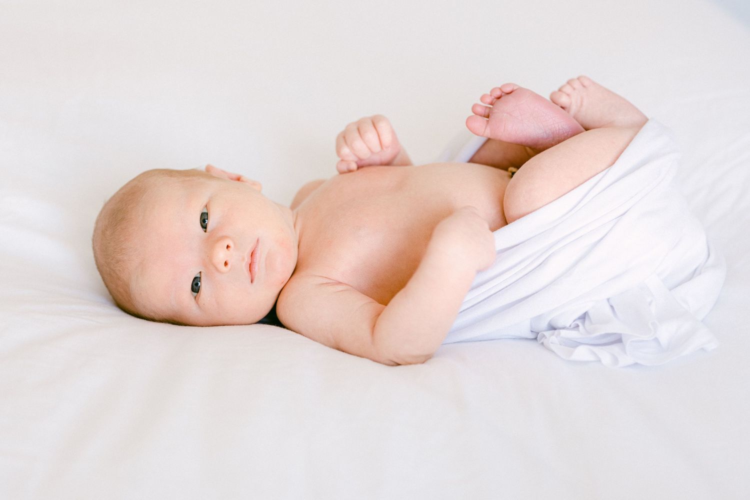 The baby is awake laying on his mom's bed in Layton Utah, Davis County.