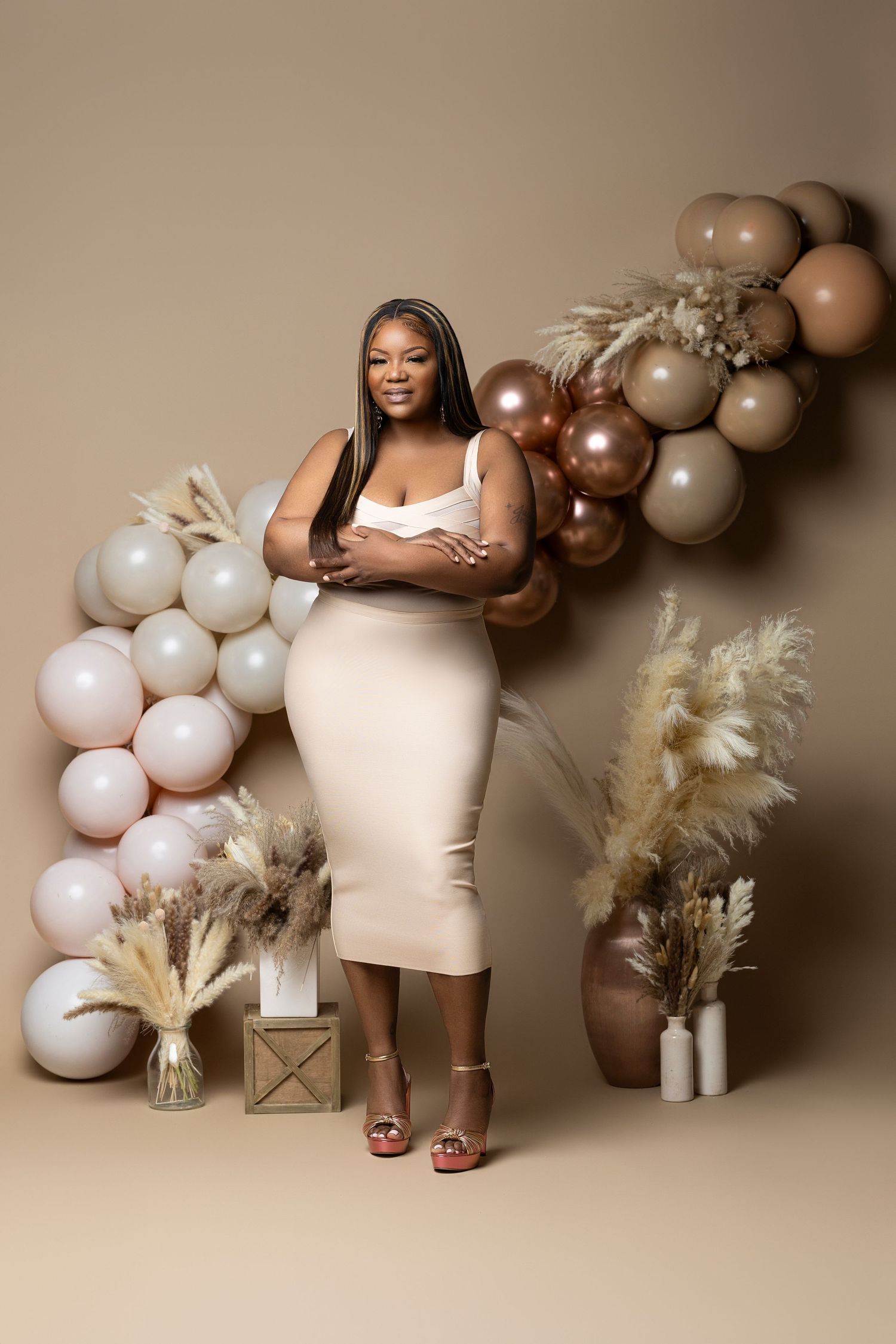 Maternity photoshoot with brown and white balloon arch and pampas grass decorations against neutral backdrop.