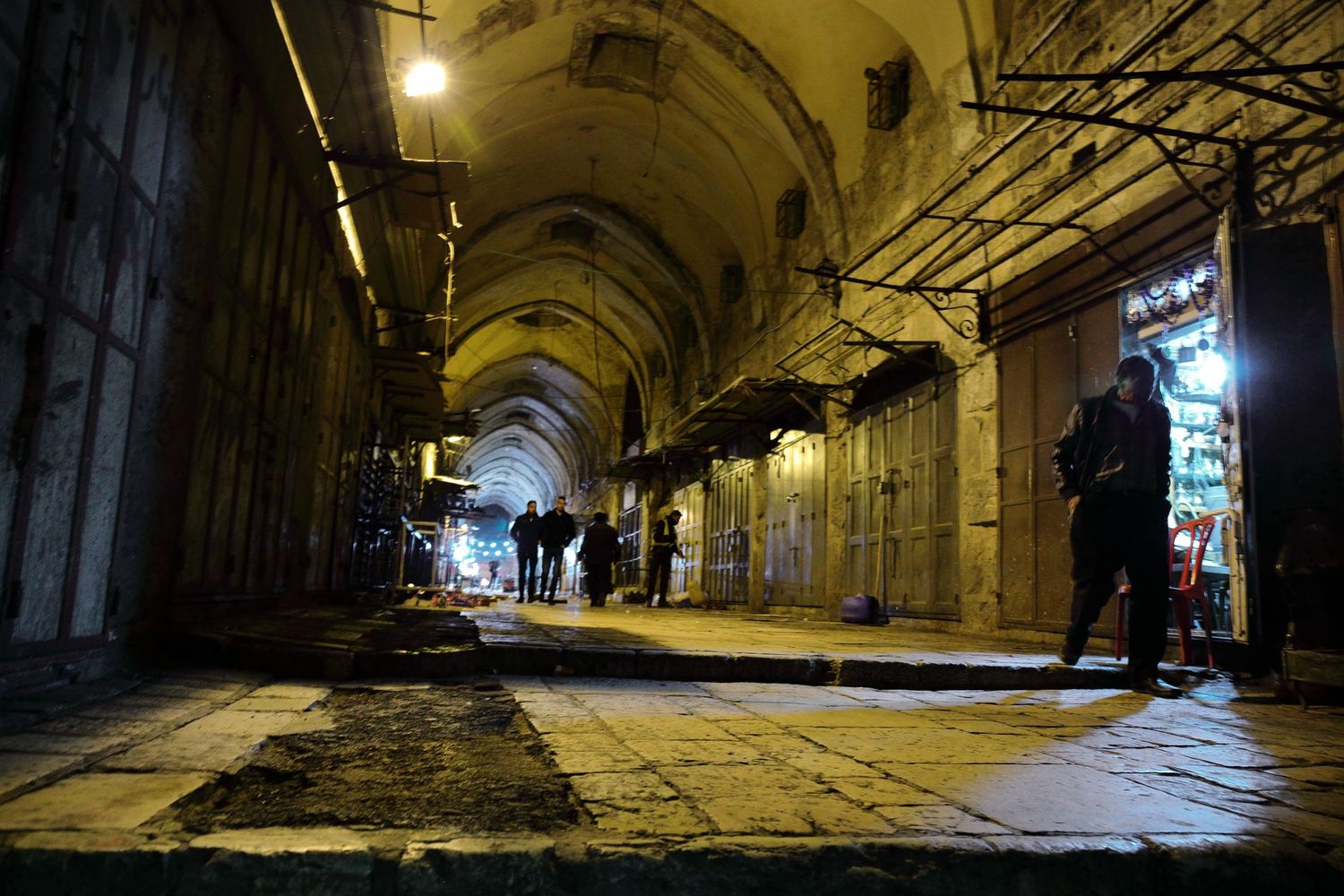 Dimly lit ancient stone arcade with vaulted ceiling and scattered pedestrians.