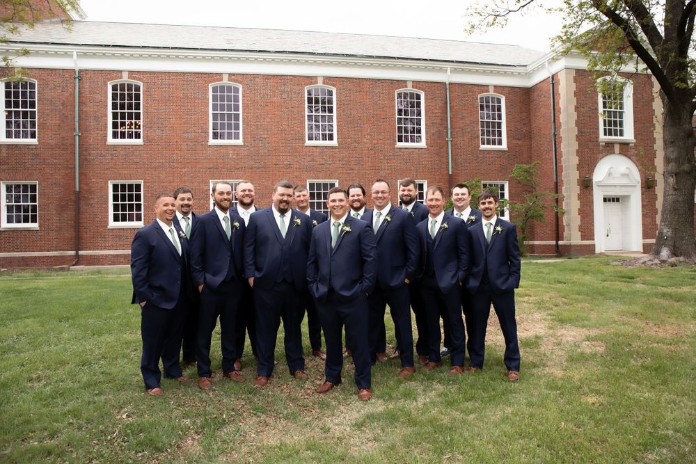 Groomsmen in navy suits pose for formal photo outside brick building.