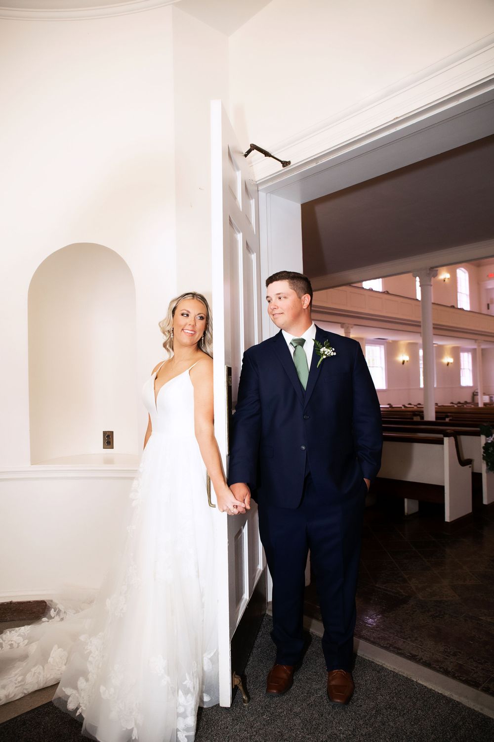 Newlyweds pose together in white church interior with classic architecture.