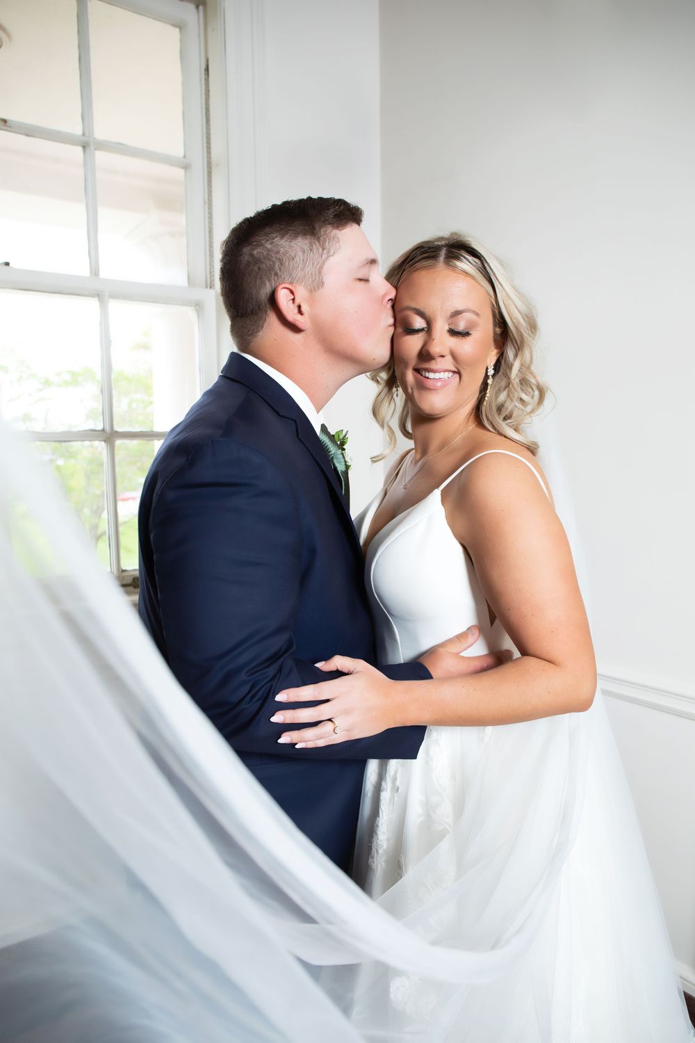 Romantic wedding portrait with flowing white veil by a bright window.