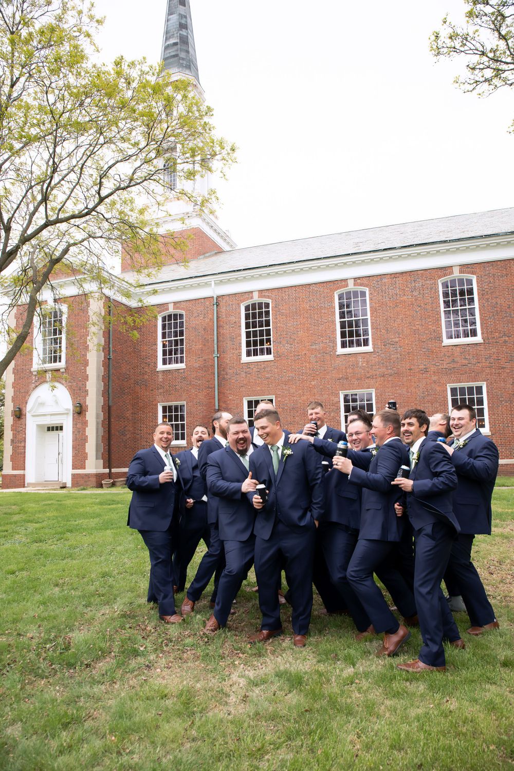 Groomsmen in navy suits celebrate outside historic brick church.