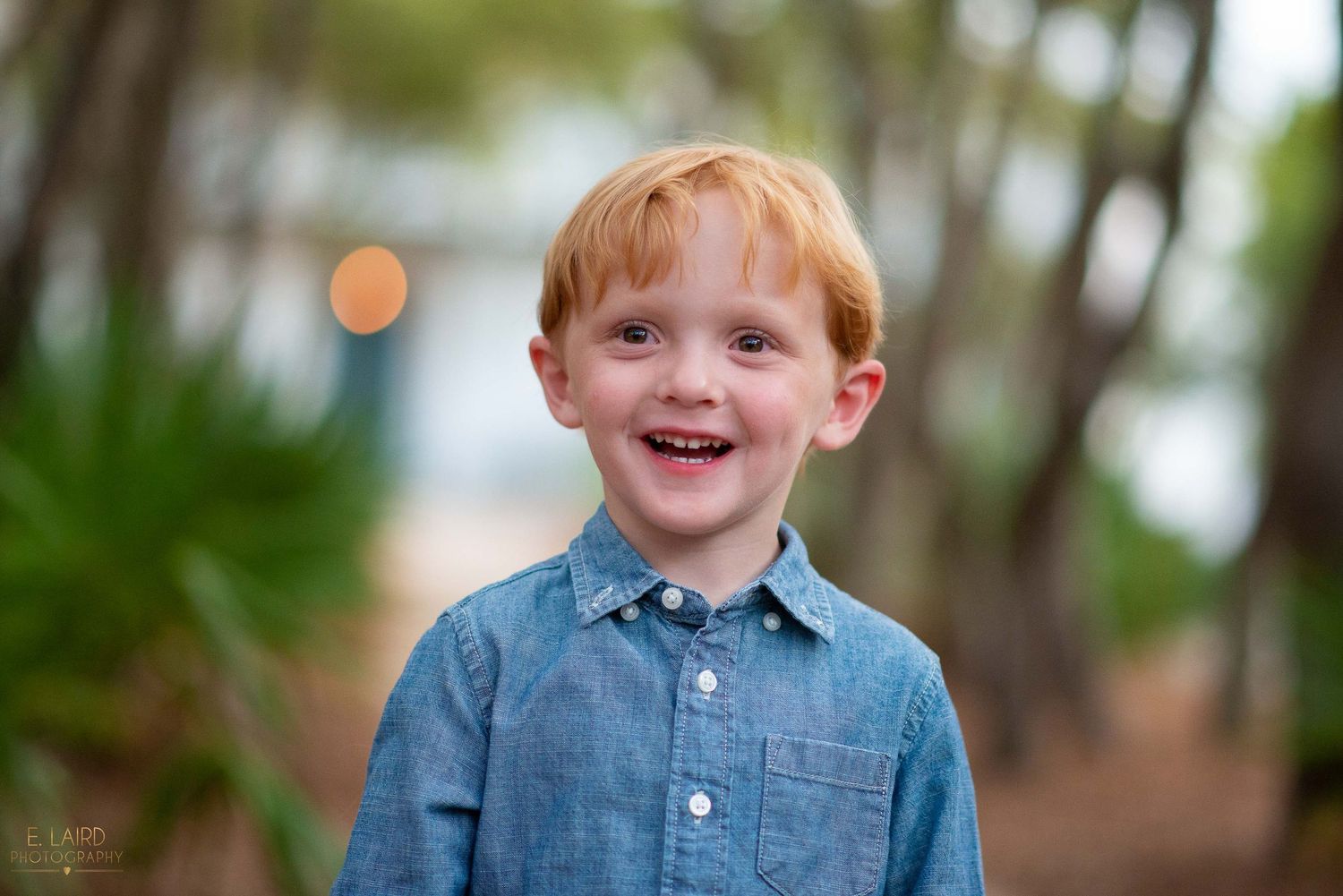 Child wearing blue button-down shirt smiling outdoors.