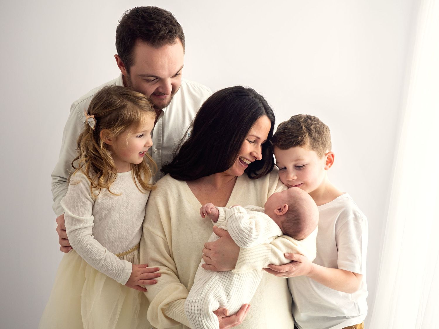 A young family of five pose together in a white studio for photographs with their newborn baby.