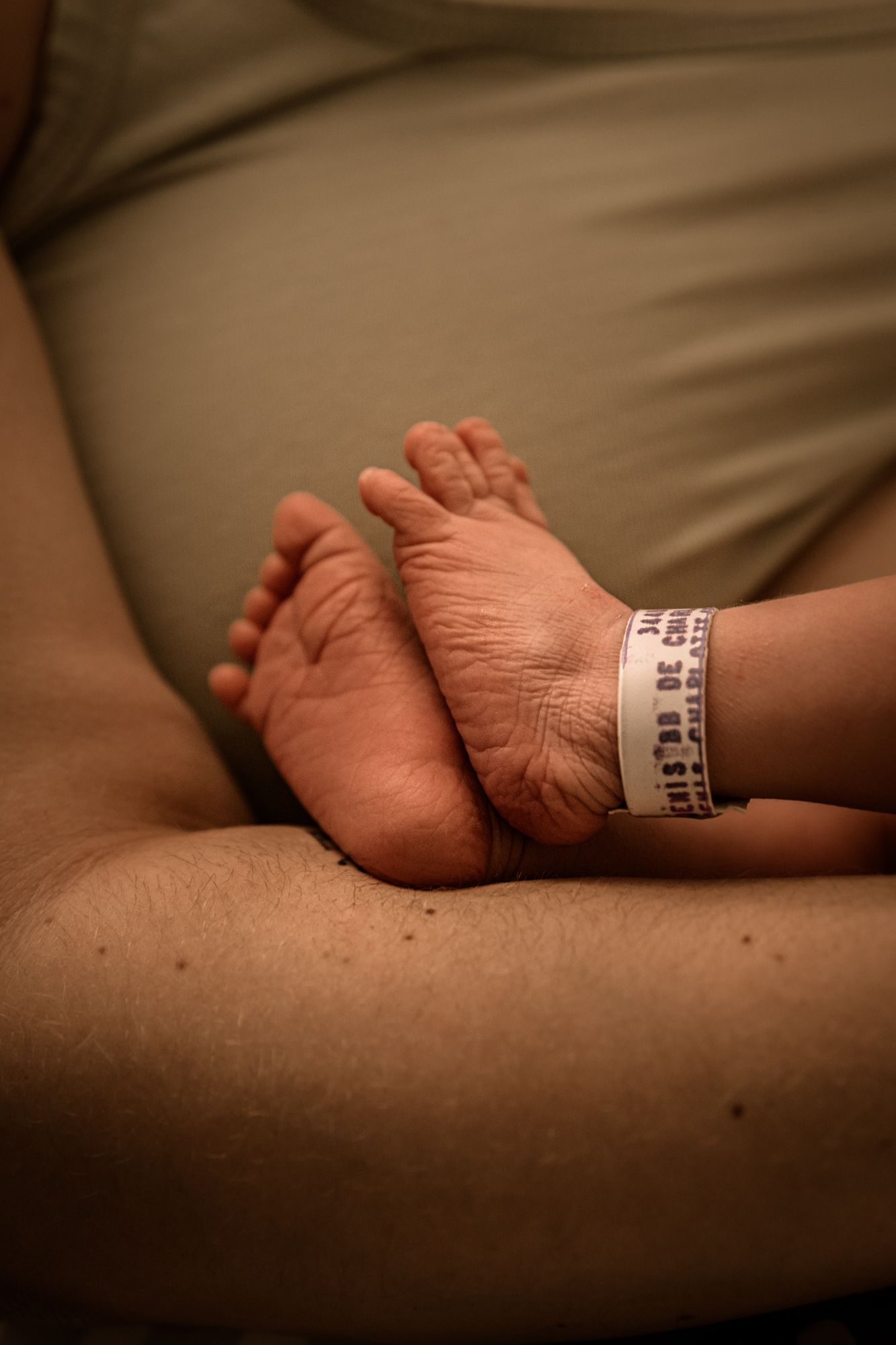 Close-up of newborn baby feet with hospital ID bracelet resting on brown leather surface in warm lighting.