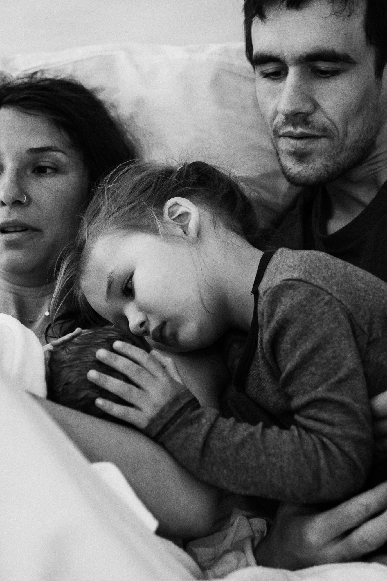 A young family sleeping together in black and white, with a child nestled between parents in a tender moment.