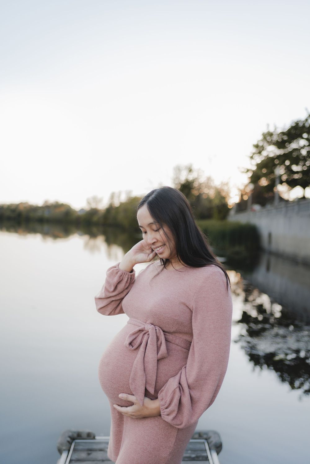 Person in pink sweater standing on dock overlooking peaceful water.