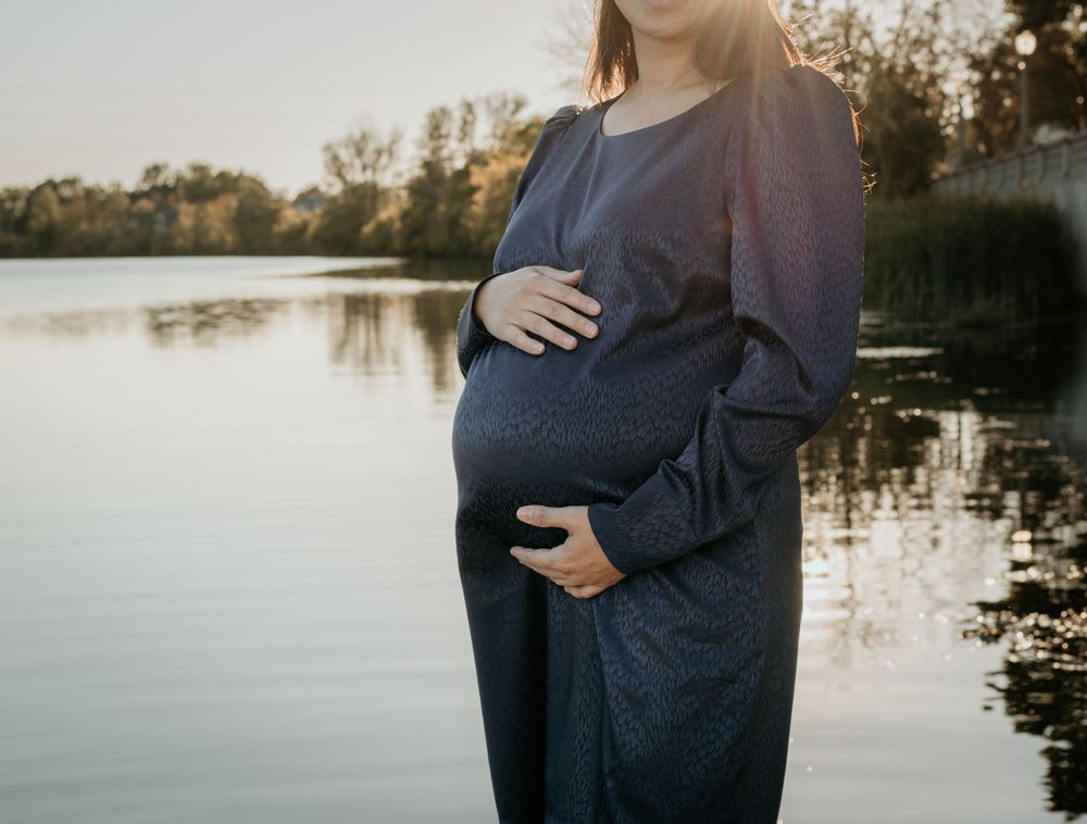 Maternity photos at sunset by a lake showing silhouetted couple embracing.