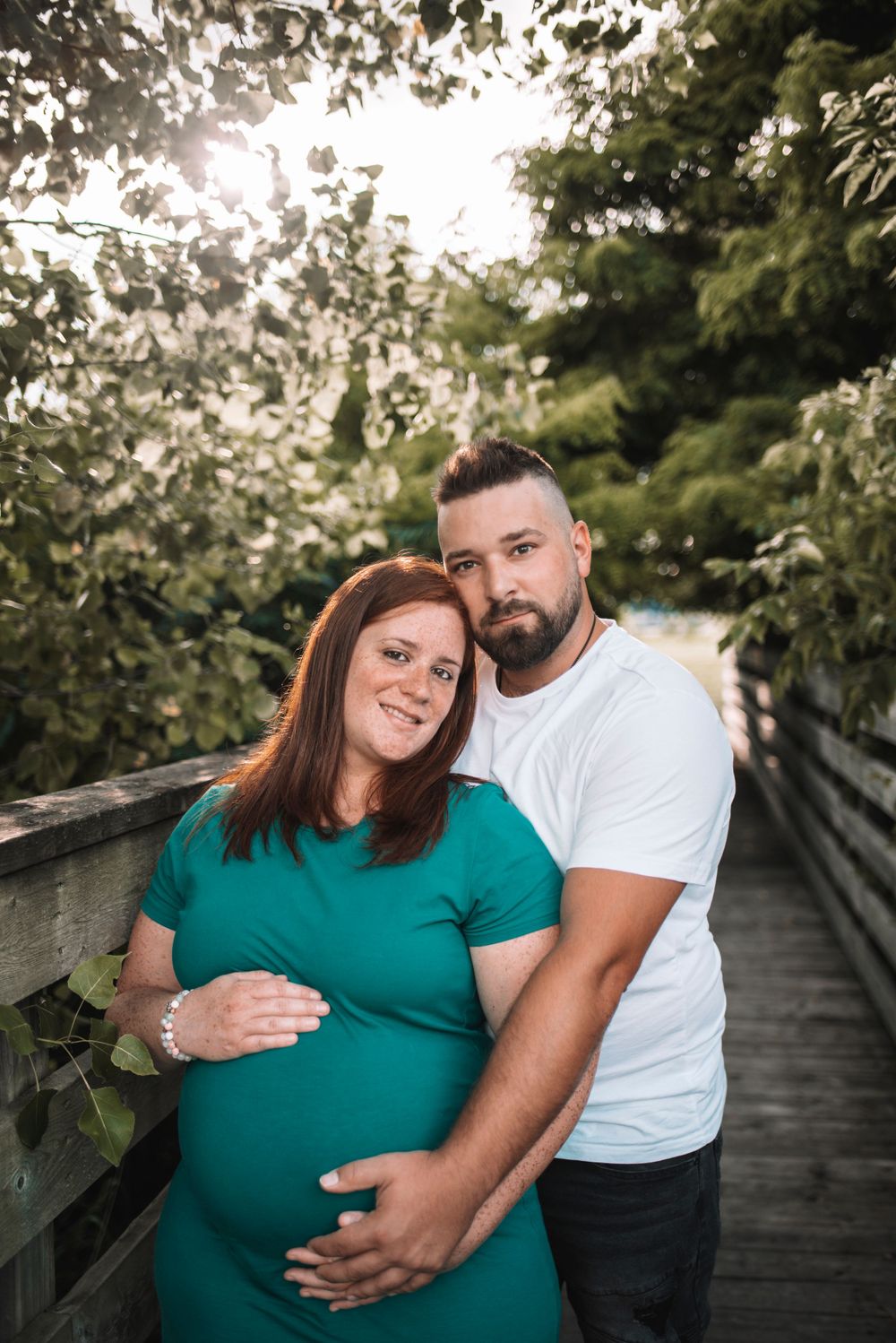 Maternity photo session in a garden setting with couple in teal and white outfits.