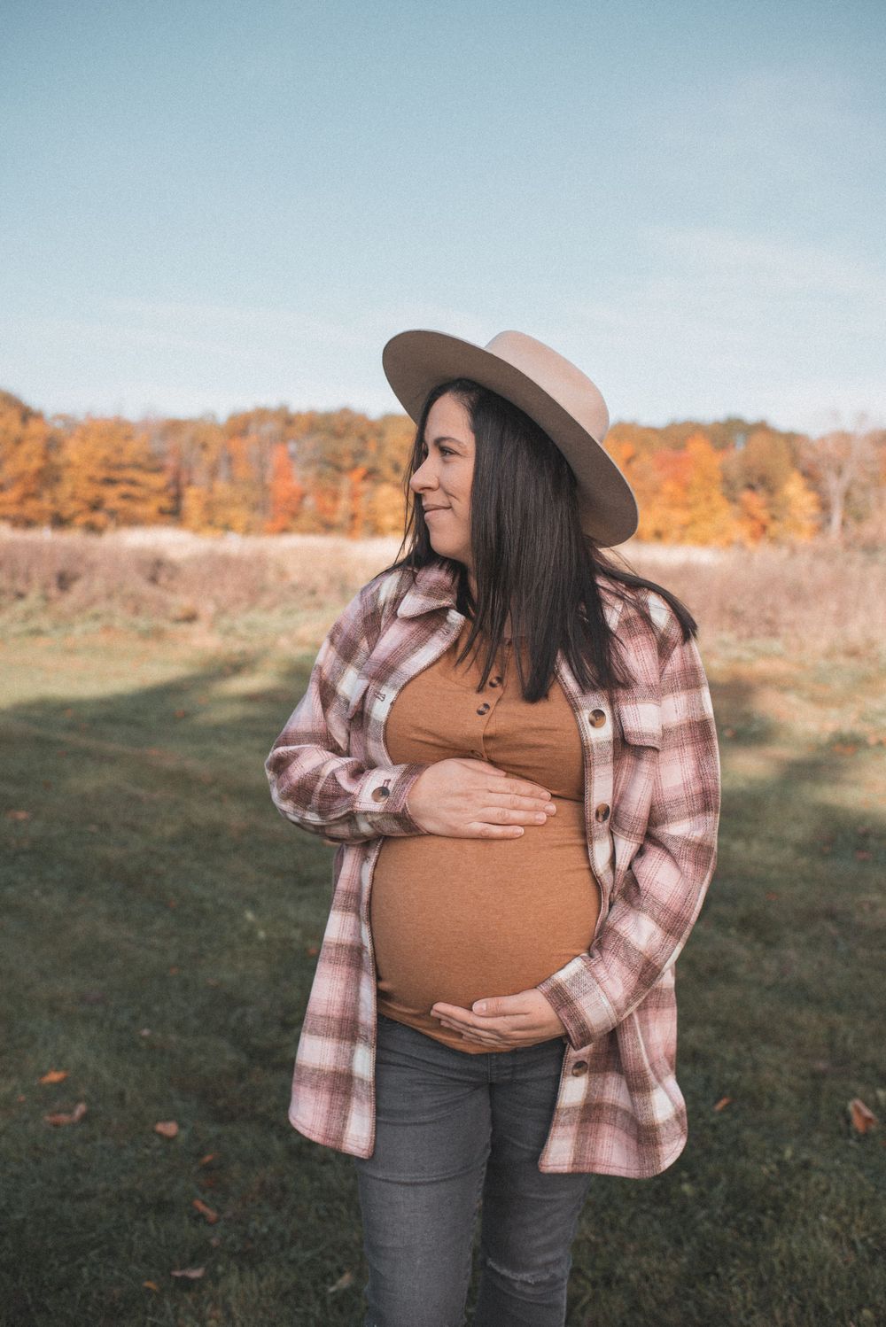 Woman wearing plaid shirt and hat posing in autumn field setting.