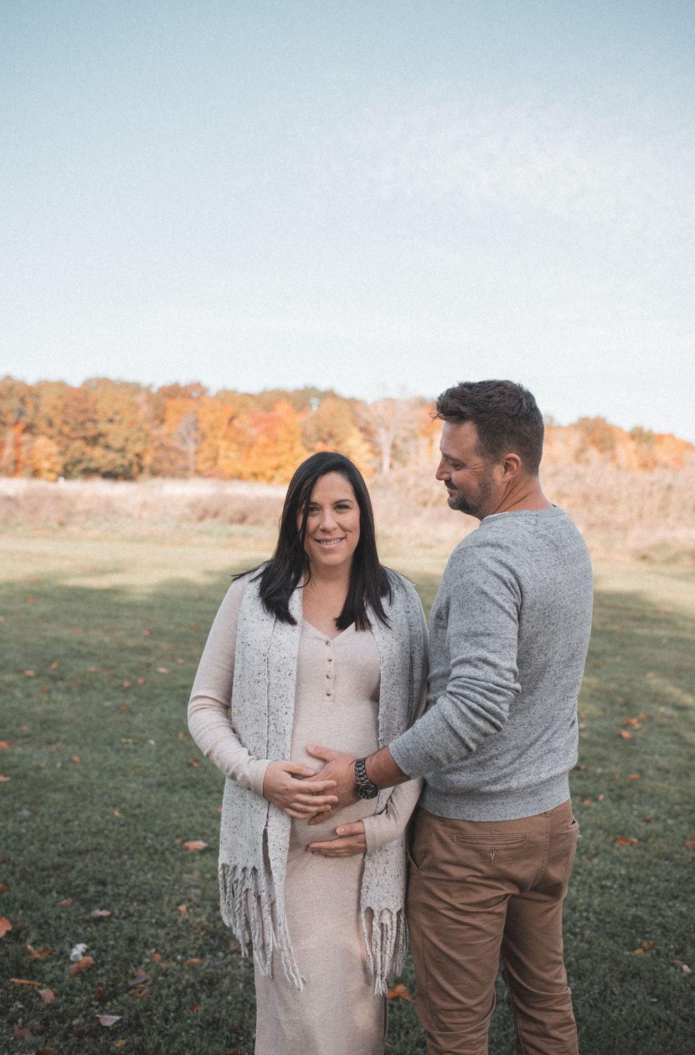 Couple embracing in field during autumn with colorful fall foliage in background.